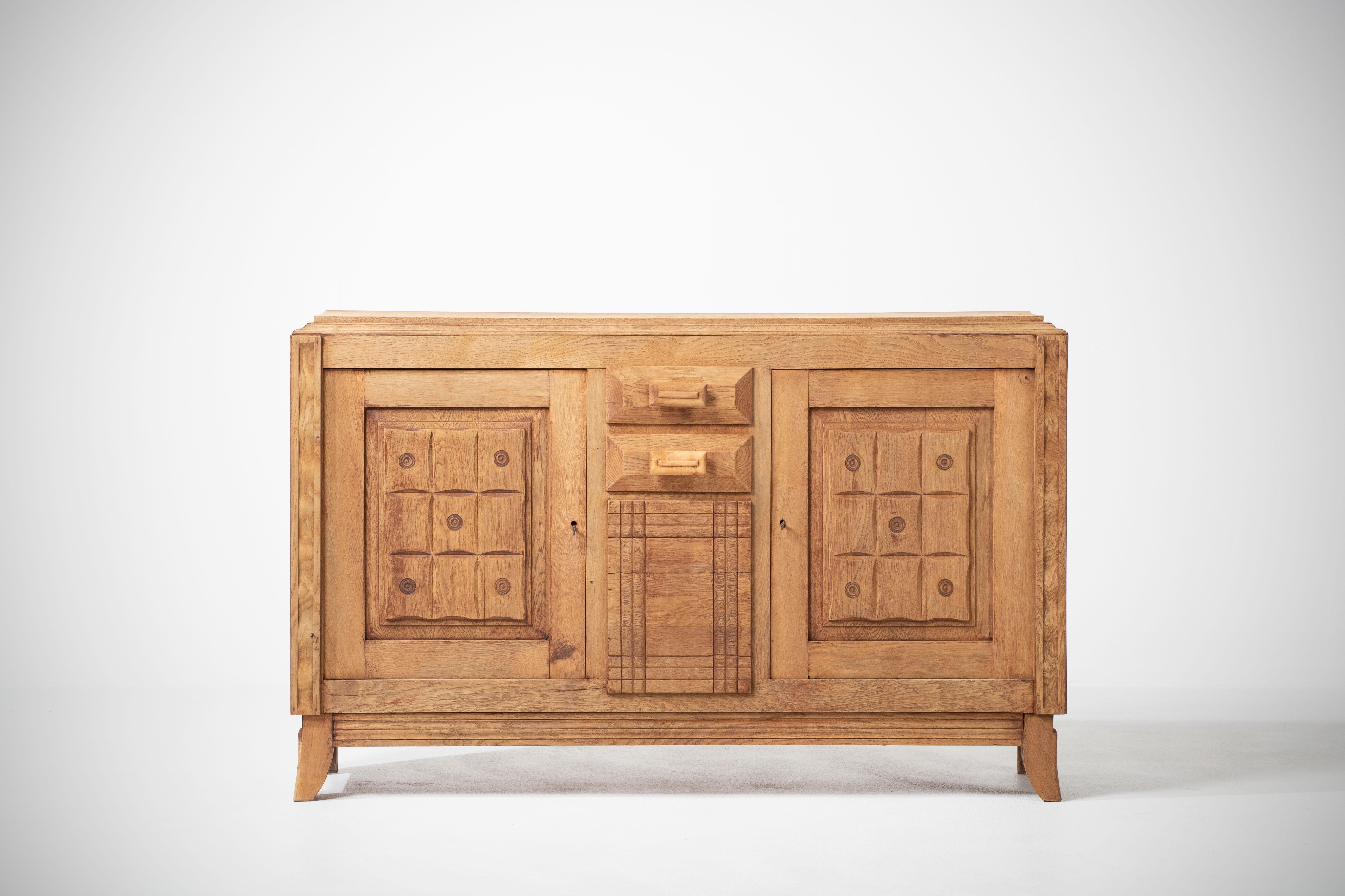Credenza, solid oak, France, 1940s, in stylo of Charles Dudouyt.
Large Art Deco Brutalist sideboard. 
The credenza consists of two storage facilities covered with very detailed designed door panels, in the center a floral sculpture.
 