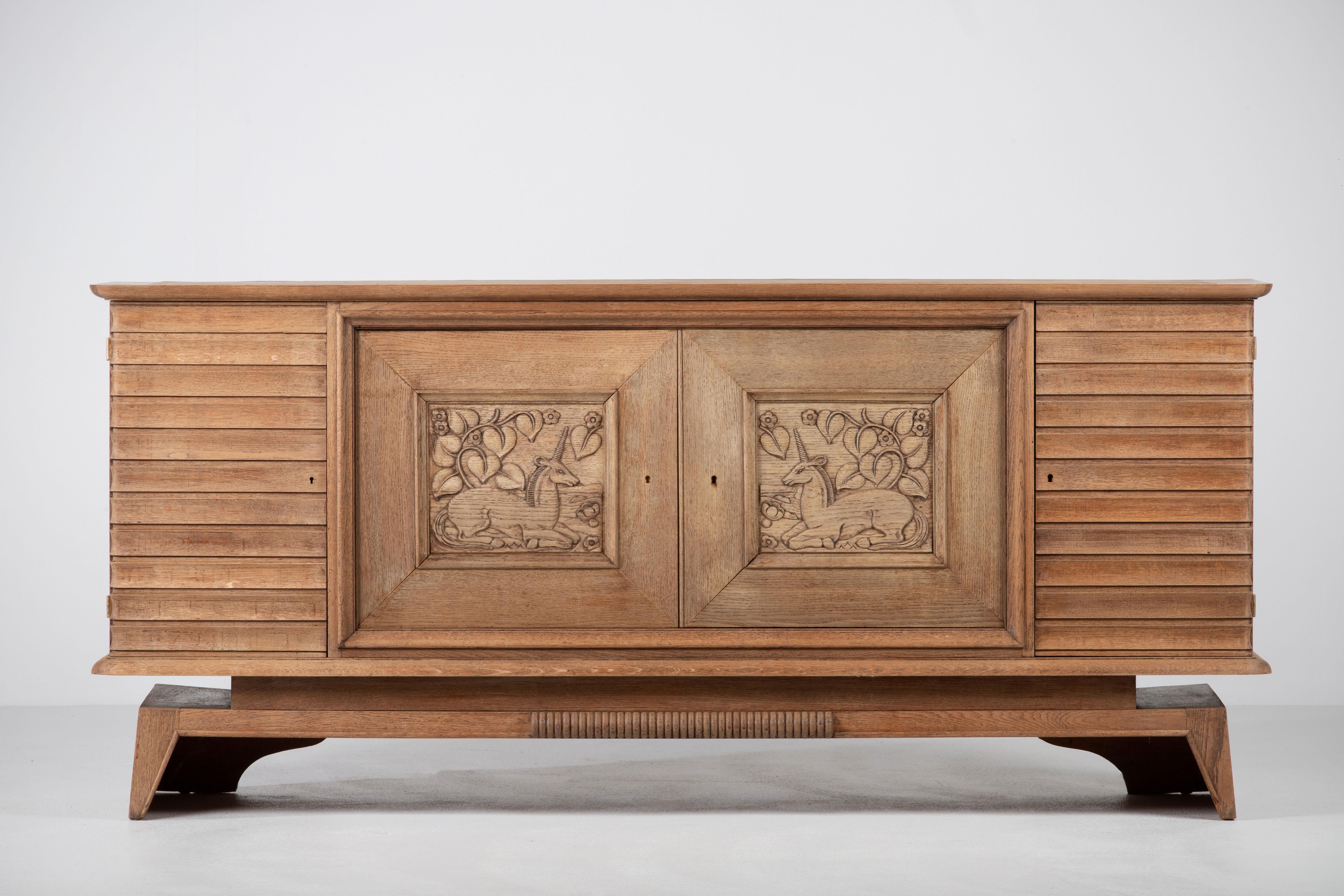 Credenza, solid oak, France, 1940s, attributed to Charles Dudouyt.
Large Art Deco Brutalist sideboard. 
The credenza consists of two storage facilities covered with very detailed designed door panels, in the center a floral sculpture.
 