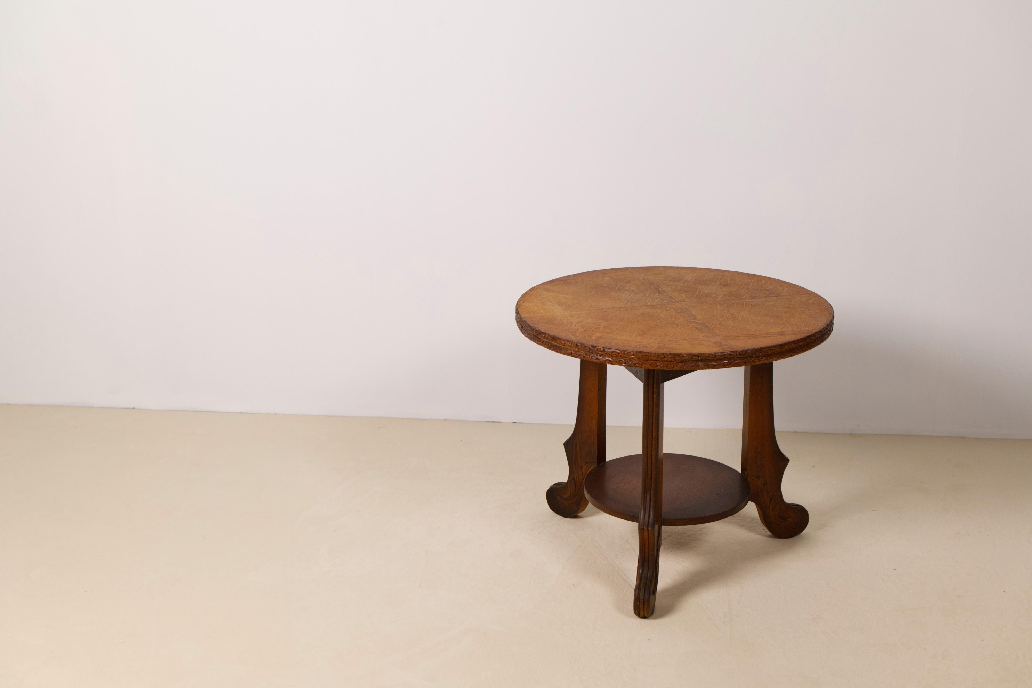 Art Deco two-tiered side table in oak, Belgium, 1930s.

A finely crafted table features a circular top with a hand-carved edge and an intricate inlaid oak pattern, reflecting the geometric elegance of the period. The lower tier is supported by