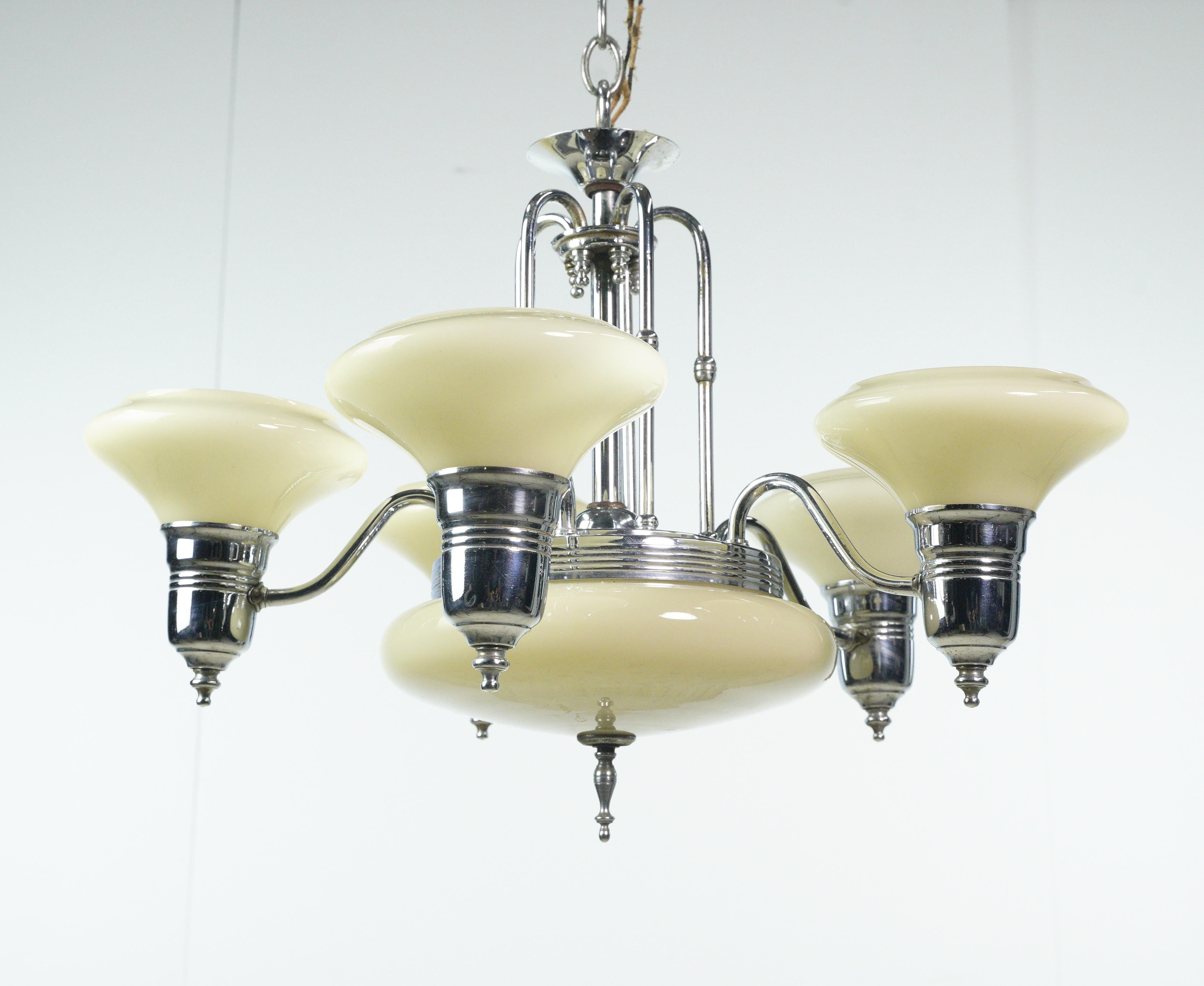 Dieser Art-Deco-Kronleuchter aus den 1950er Jahren ist eine stilvolle Leuchte mit weißen Glasschirmen, einem weißen Glasfuß und einer fünfarmigen Stahlrahmenkonstruktion. Es fängt die Essenz des Art-Déco-Designs ein und verleiht jedem Raum einen