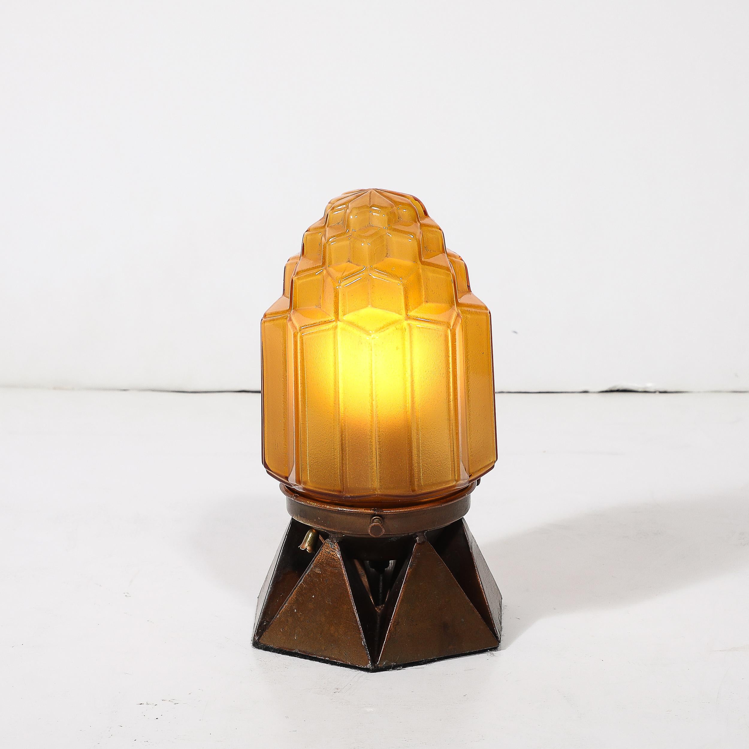 Questa splendida lampada da tavolo Art Déco, realizzata in America intorno al 1935, è un perfetto esempio dello stile a grattacielo che definiva il design dell'epoca. Il vetro rosa modellato e smerigliato presenta una tonalità morbida e luminosa che