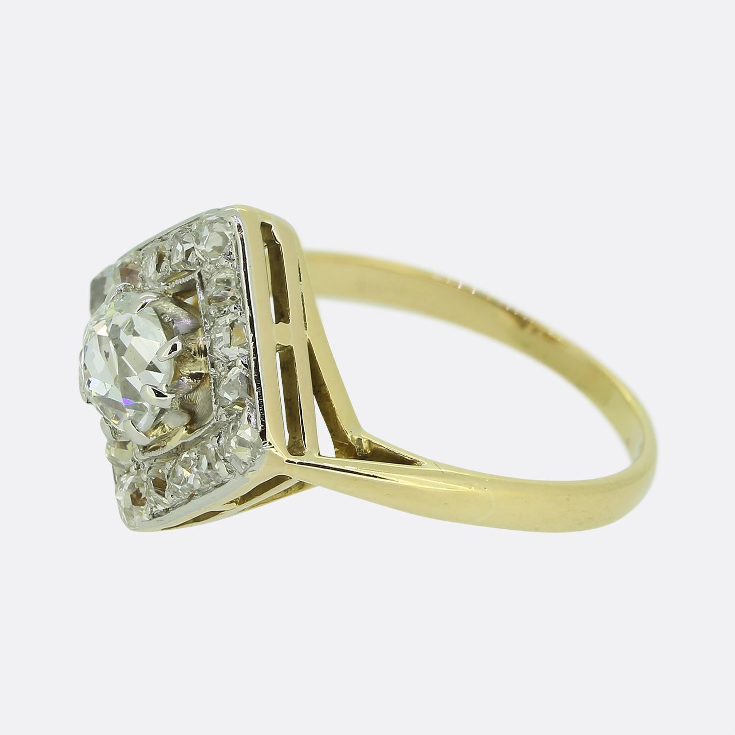 Hier haben wir einen auffälligen Art-Déco-Cluster-Ring, in dessen Mittelpunkt ein antiker Diamant im Kissenschliff steht. Dieser Hauptstein sitzt leicht erhöht auf einem offenen Hintergrund, bevor er von einem quadratischen Rahmen aus kleineren,