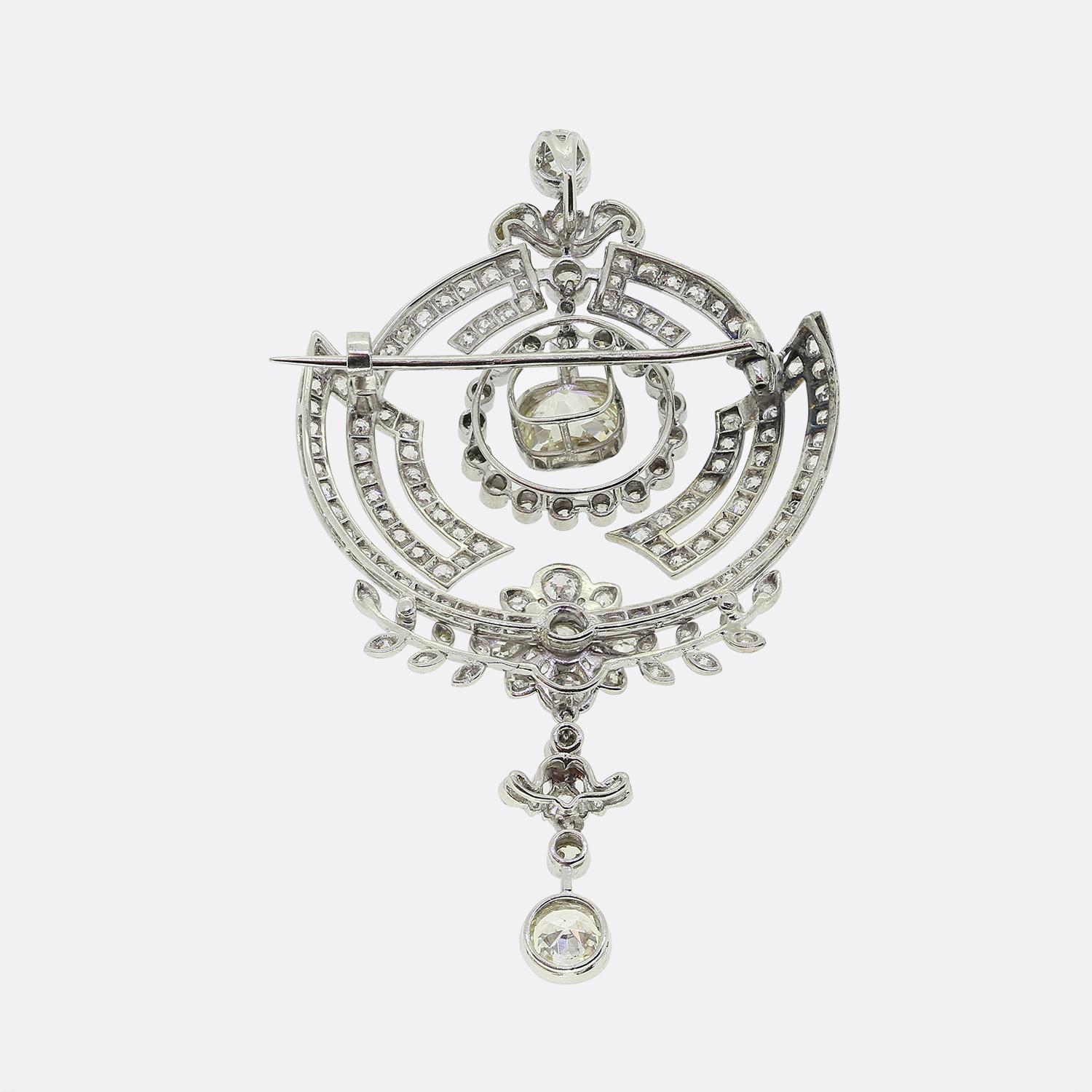 Aquí tenemos un reluciente broche con gota de diamantes elaborado durante el apogeo del movimiento Art Déco. Este intrincado diseño presenta un diamante de talla antigua centralizado rodeado de arcos concéntricos de diamantes más pequeños. Debajo de