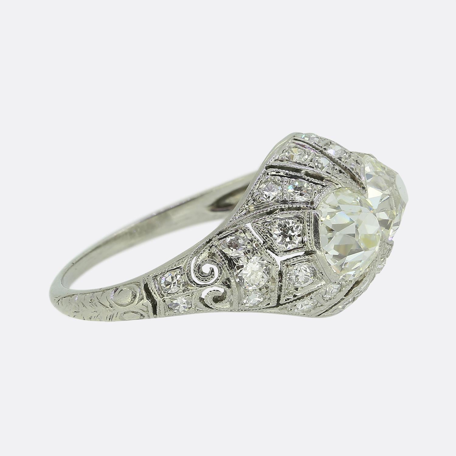 Here we have a sensational ring dating back to early stages of the Art Deco movement. The platinum piece showcases two captivating old mine cut white diamonds, set side by side atop an intricate filigree backdrop. This ornate open design acts as the