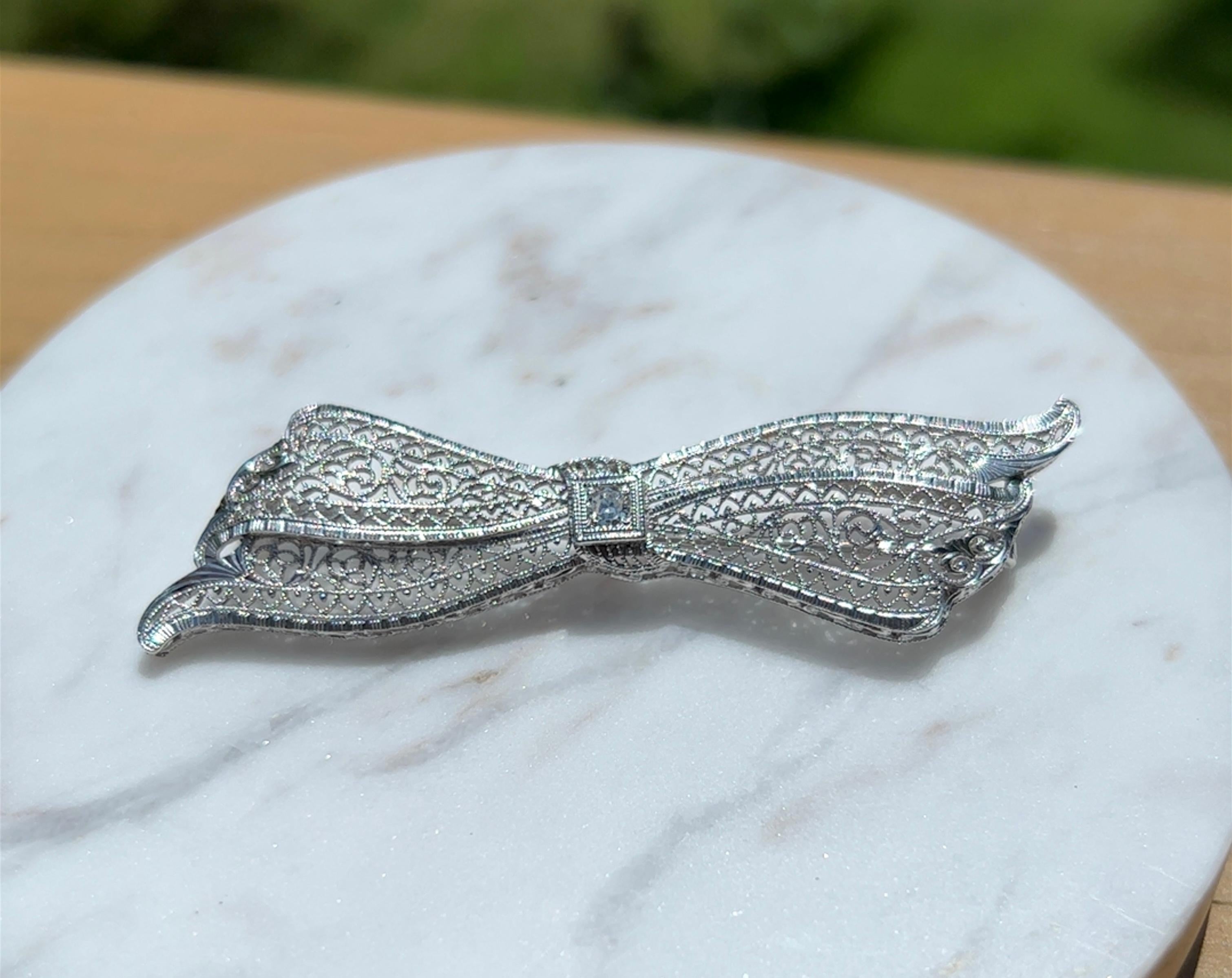 One 14 karat white gold Art Deco filigree bow design pin, set with one (1) old European cut diamond, approximately 0.07 carat with I/J SI1 clarity.  The pin measures 2.5 inches long and 0.25 of an inch wide. The pin weighs 5.4 grams and is complete