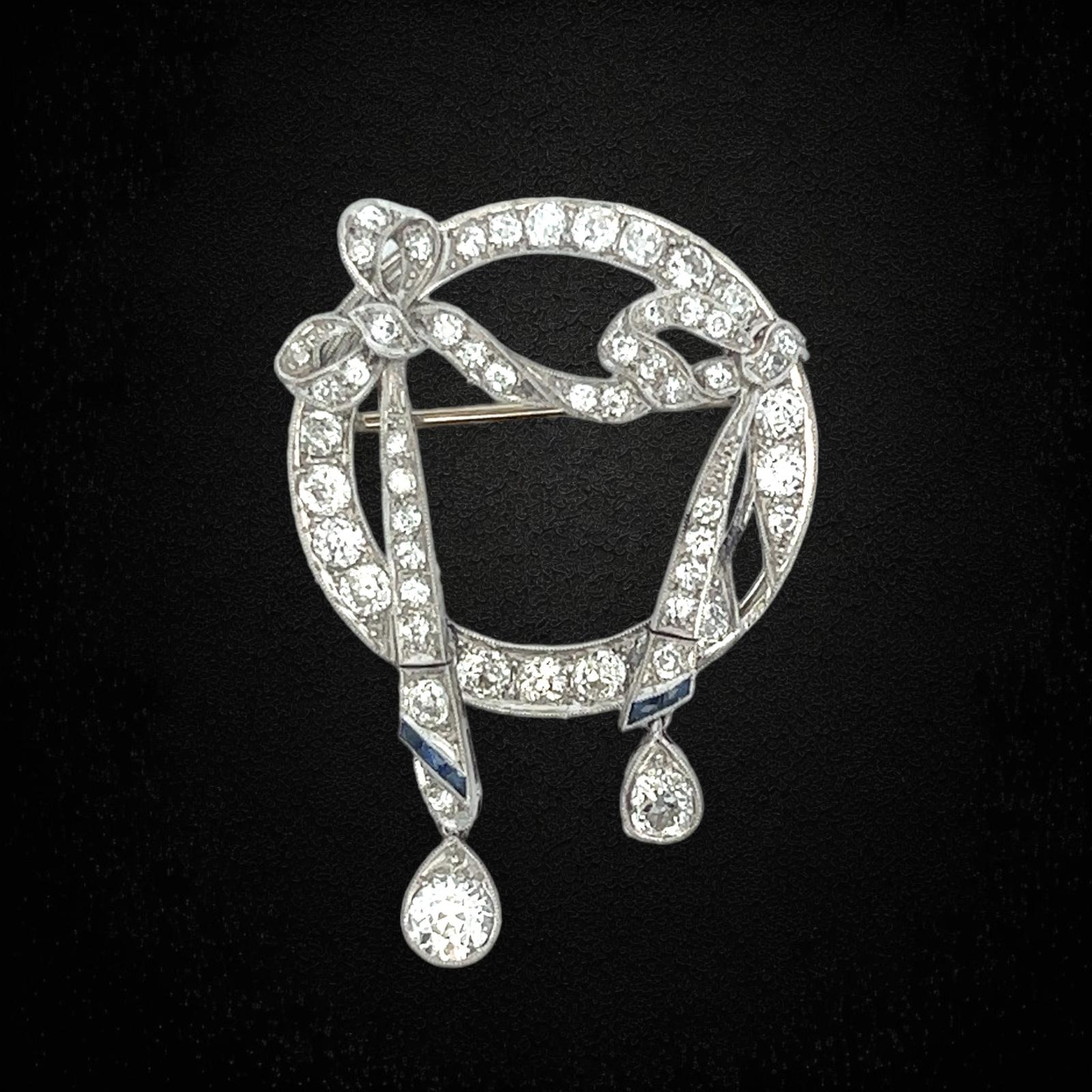 Original Art Deco diamond sapphire bow brooch handcrafted in platinum. The brooch features 2 Old European cut diamond drops weighing approximately 1.00 carat total weight and another 52 old Europan cut diamonds weighing approximately 3.50 carat