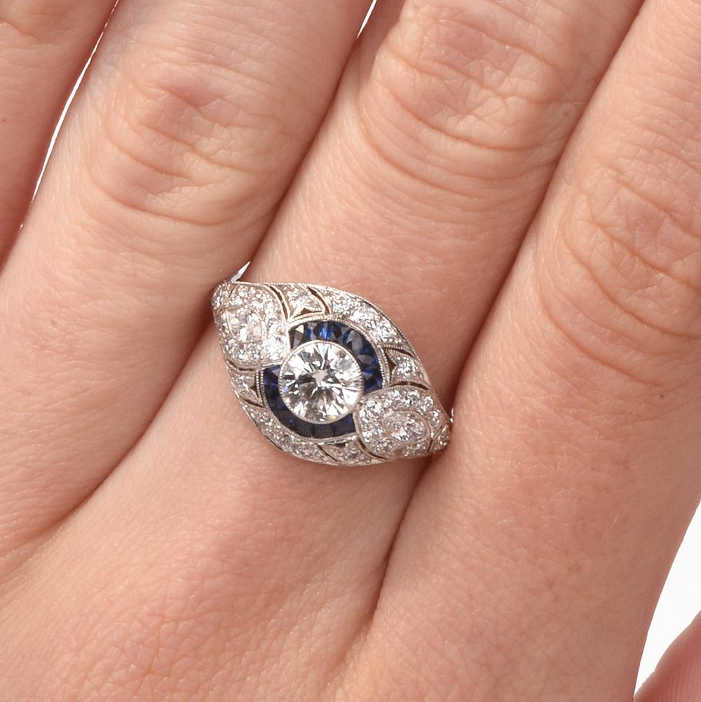 This stunning Art Deco inspired diamond and blue sapphire ring is crafted in solid platinum, weighing 4 grams and measuring 12mm x 5mm high. Showcasing one prominent bezel-set, old European diamond weighing approximately, 0.67 carats, graded G-H