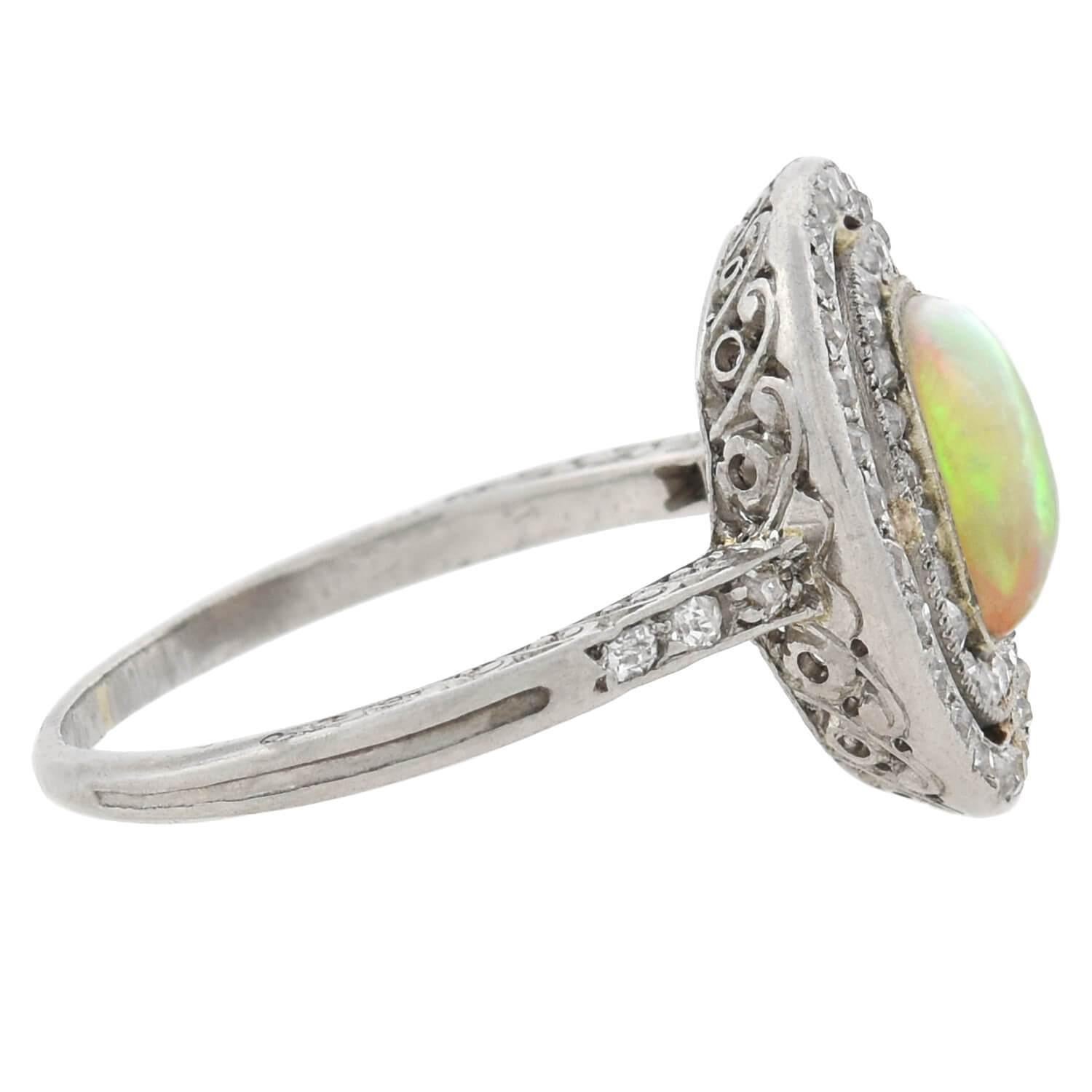 A stunning opal and diamond ring from the Art Deco (ca1920s) era! This fabulous piece is crafted in platinum and features a lovely opal cabochon bezel set at its center. The opal has an alluring quality and a vibrant multitude of colors that vividly