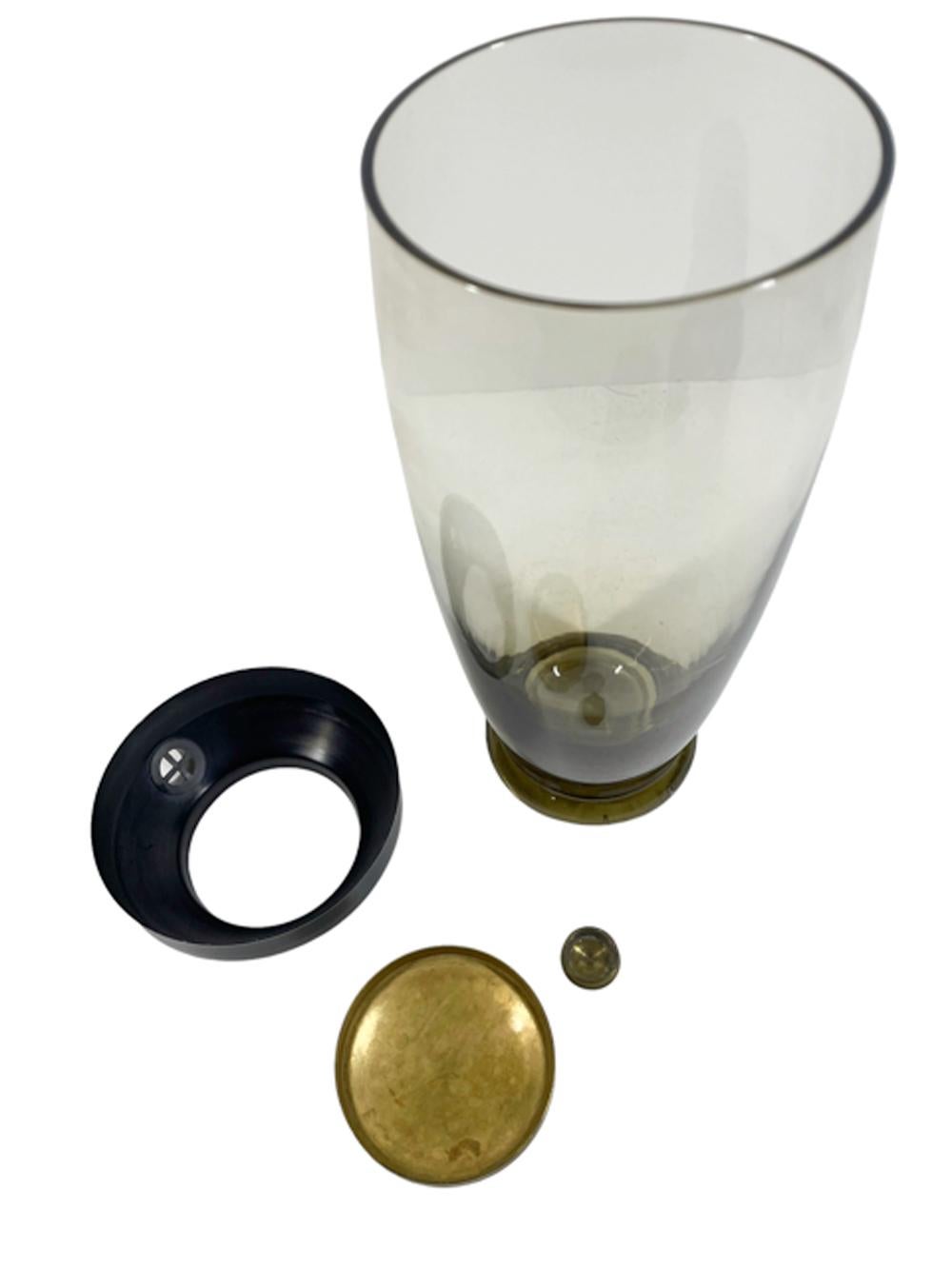 Art Deco cocktail shaker of pale olive green glass of tapered form on a thick circular foot and topped with a black enameled cover with a brass lid and pour spout cap.