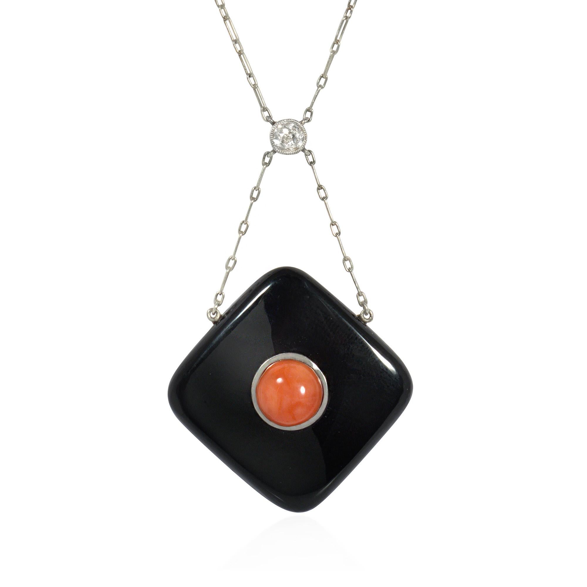 An Art Deco coral, onyx, diamond, and platinum necklace, comprised of an onyx lozenge centered by a collet-set coral cabochon, suspended by a platinum chain from a collet-set diamond with a millegrain border, the chain further embellished with coral
