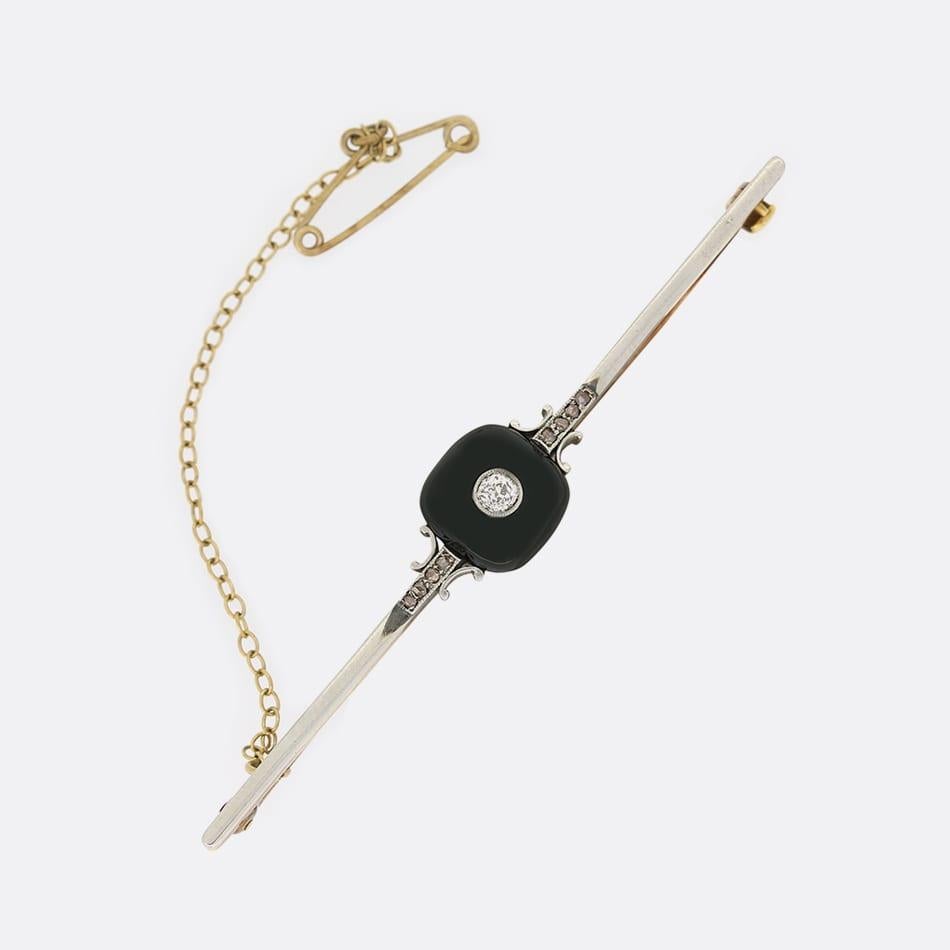 Il s'agit d'une broche Art déco en or jaune 18ct et platine. La broche a été sertie d'un onyx central en forme de dôme qui a été serti d'un seul diamant de taille ancienne. De chaque côté de l'onyx se trouvent quatre diamants taillés en rose dans