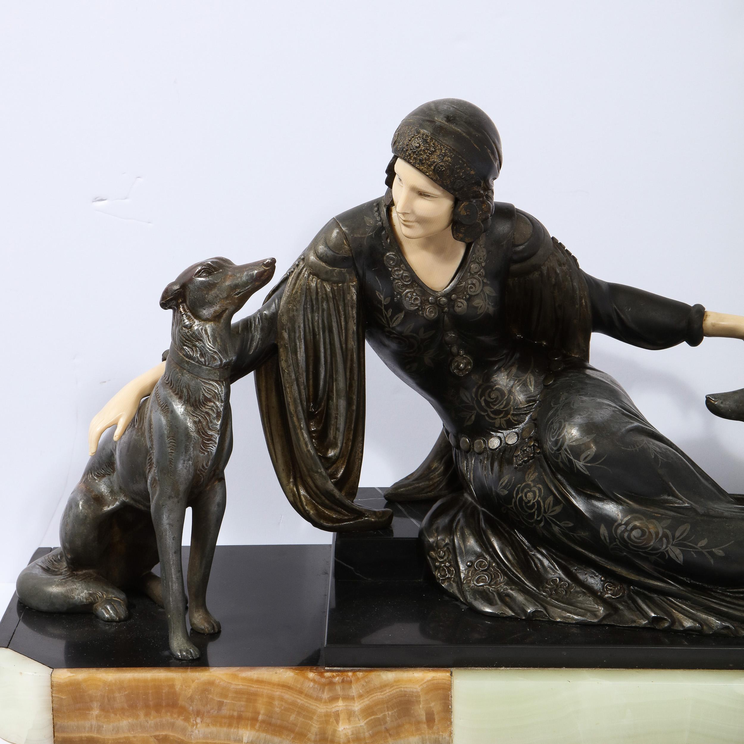 This stunning Art Deco sculpture was realized in France, circa 1930. It offers a lady in repose donning a flapper dress, flanked by two greyhound dogs in silvered pewter presented on an exotic onyx base in celadon and variegated tawny. Her hands and