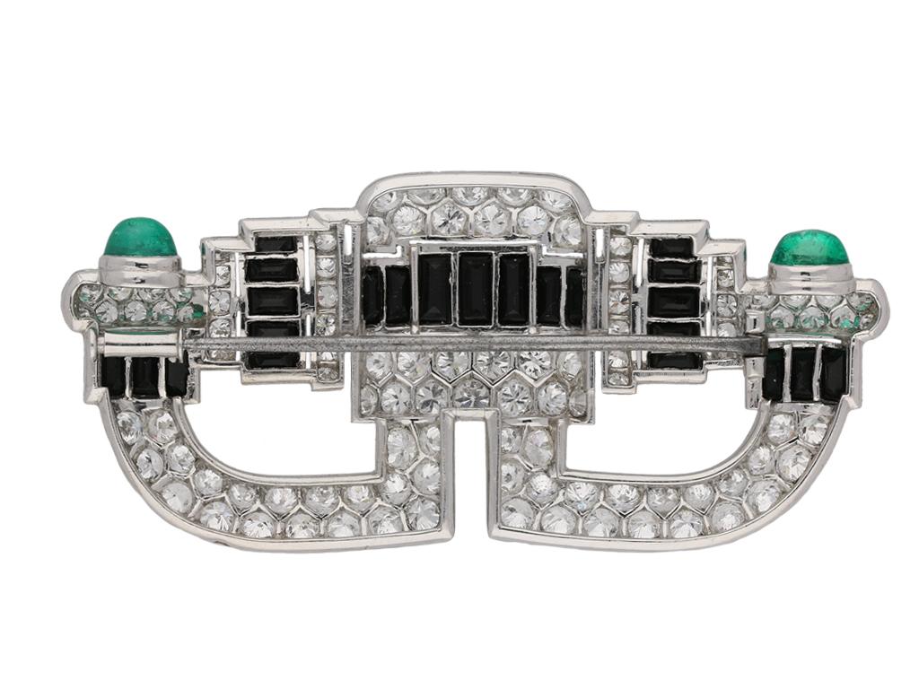 Art Deco onyx, diamond and emerald cabochon brooch. Set with one hundred and six round old cut diamonds with an approximate total weight of 10.00 carats, crossed both vertically and horizontally with bands of channel set baguette cut onyx, and the