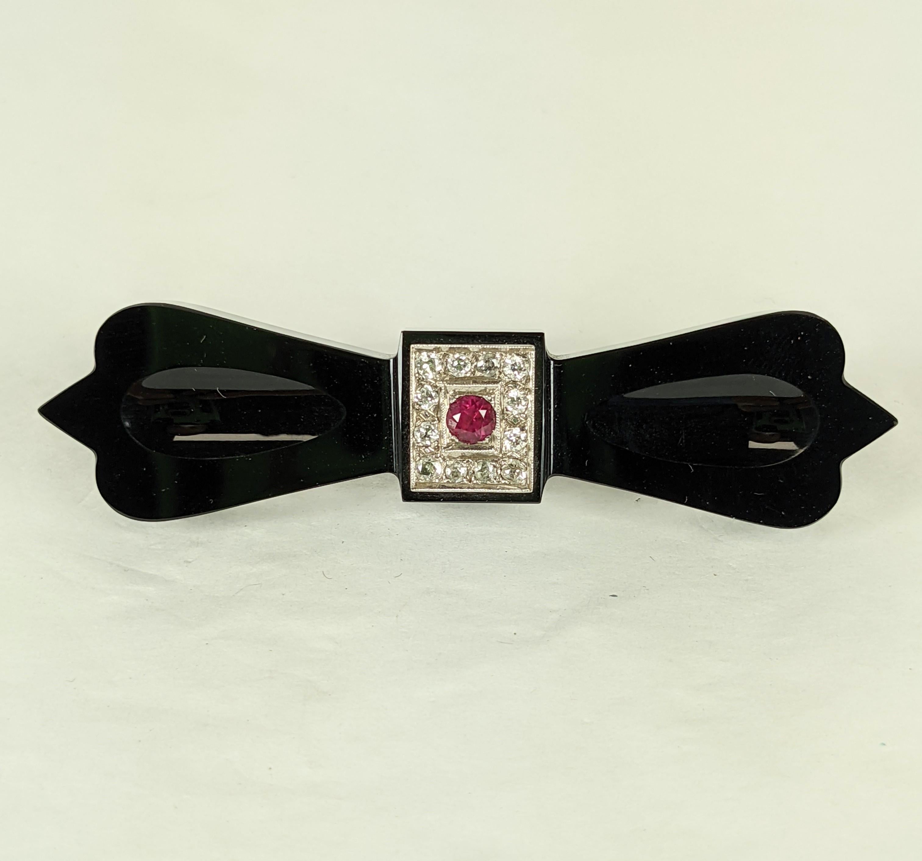 Onyx Diamond and Ruby Bow Brooch from the late 19th Century. A diamond and ruby motif has been added in the Art Deco period 40 years later. Fittings are in 14k gold. The is an effective period upcycling that adds a pop of color to a antique onyx