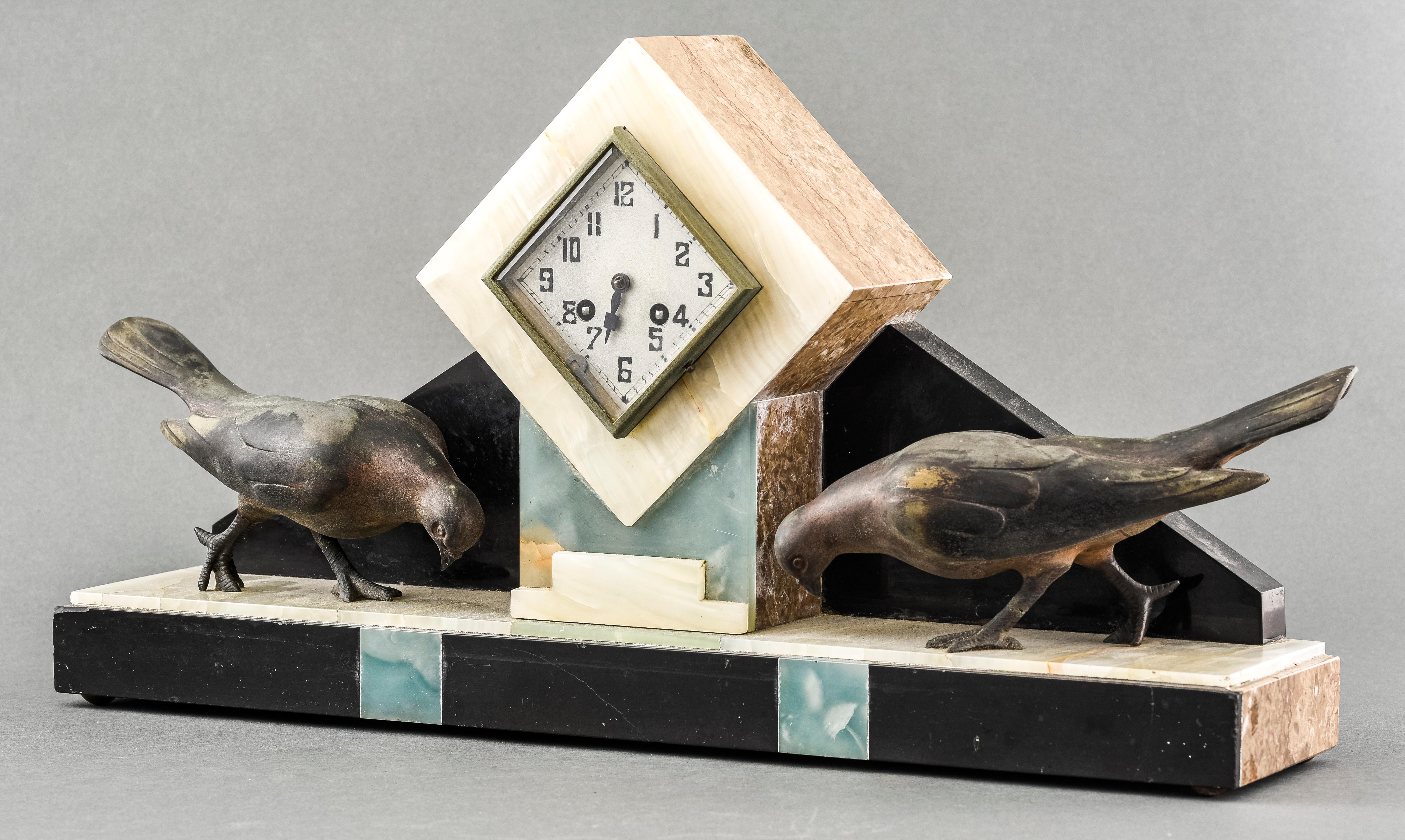 Art Deco onyx and marble three piece clock garniture, circa 1930, with patinated birds and geometric details, the clock face with Arabic numerals and two wind holes. Clock 13” H x 24” W x 5.25” D, Vases 8.25” H x 5.5” W x 4” D.
