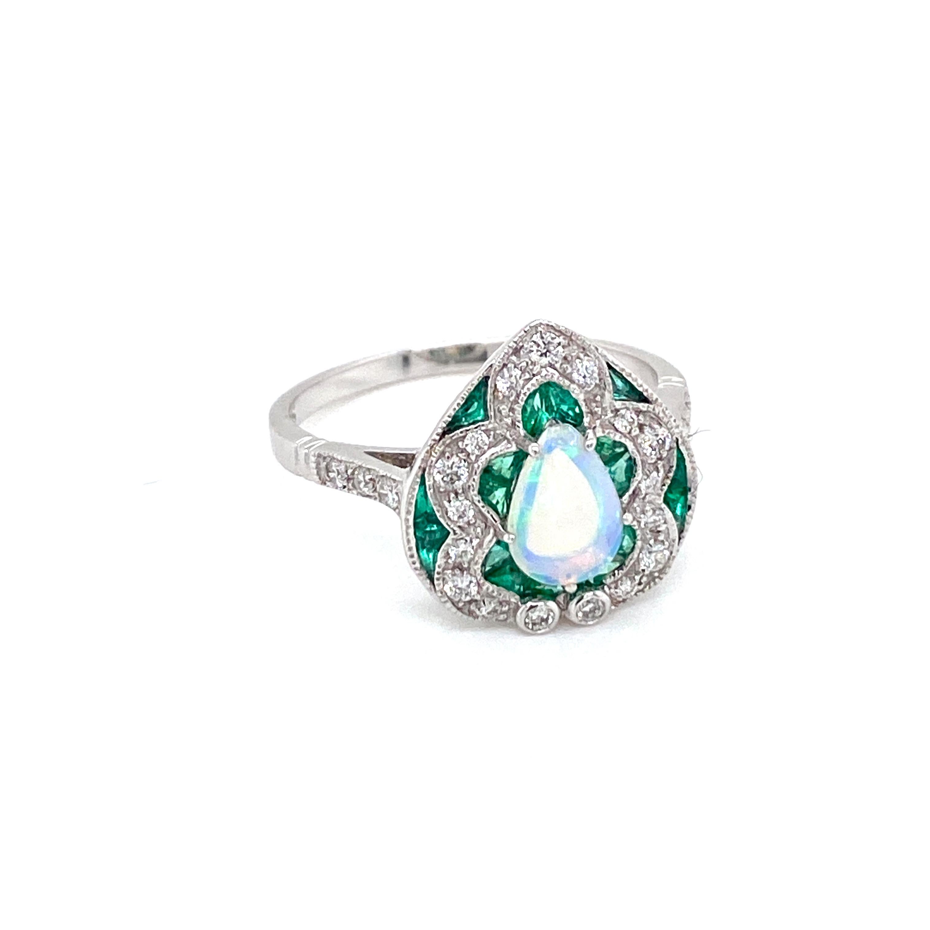Beautiful Gold handmade Art Deco style ring.
It is set in 14k white Gold featuring a large sparkling vivid Opal in the center, weight 0,50 ct., surrounded by 0,60 ct. custom cut natural fine Emeralds and Round brilliant cut diamonds totaling 0.40