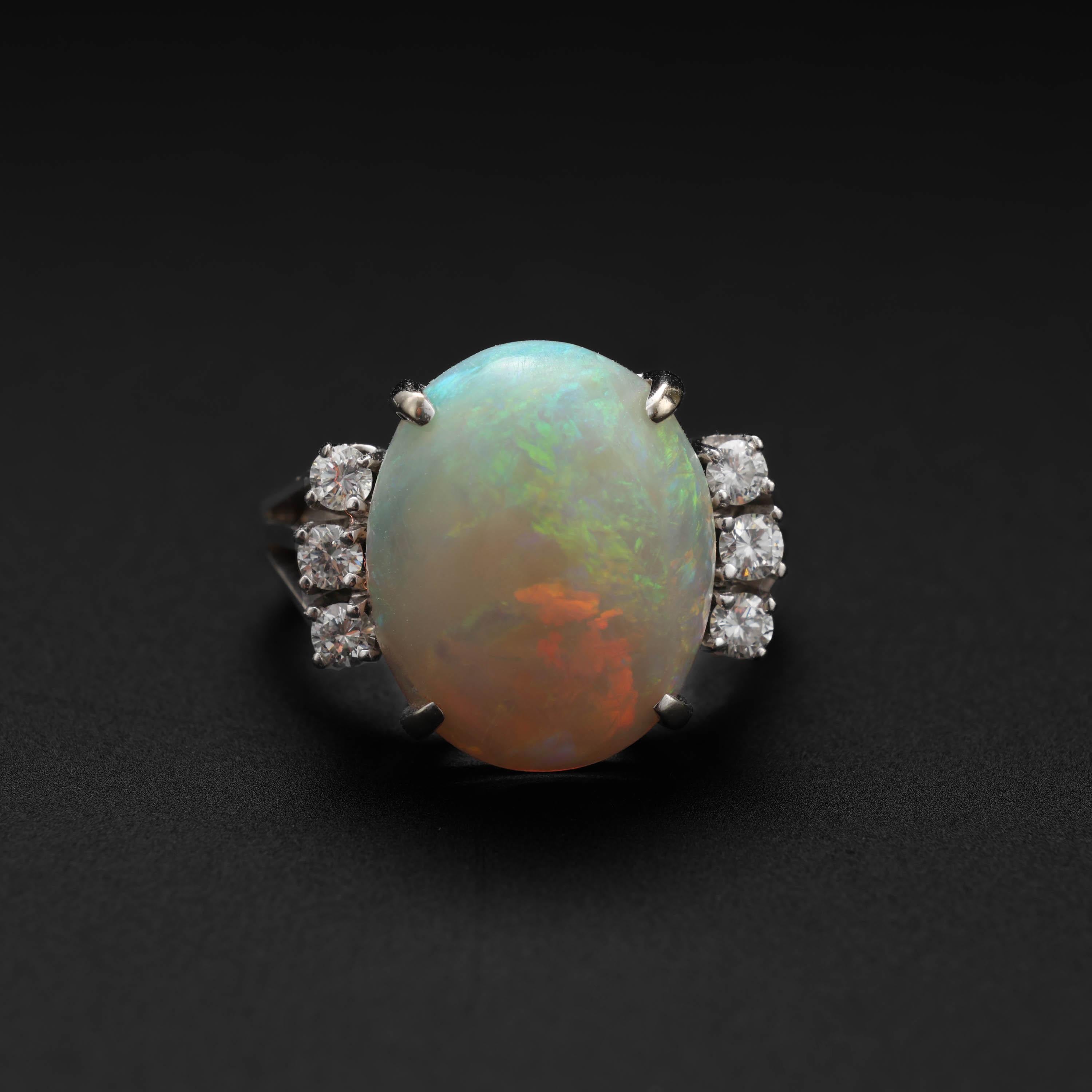 This Art Deco opal and diamond ring features a glowing, ethereal certified natural Australian crystal opal weighing approximately 6.5 carats is adorned on either side by a trio of small bright white diamonds that total approximately .25 carats in