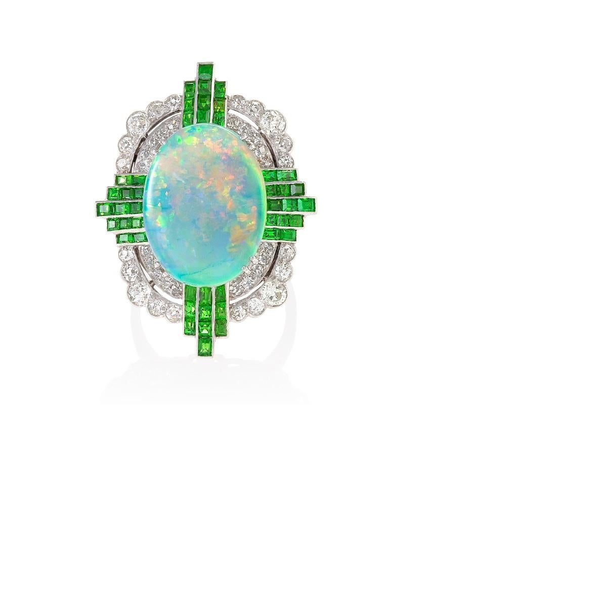 An Art Deco platinum ring with white opal, demantoid garnets and diamonds. The ring centers on a white opal that has an approximate weight of  3.77 carats. It is surrounded by  47 calibre-cut demantoid garnets with an approximate total weight of