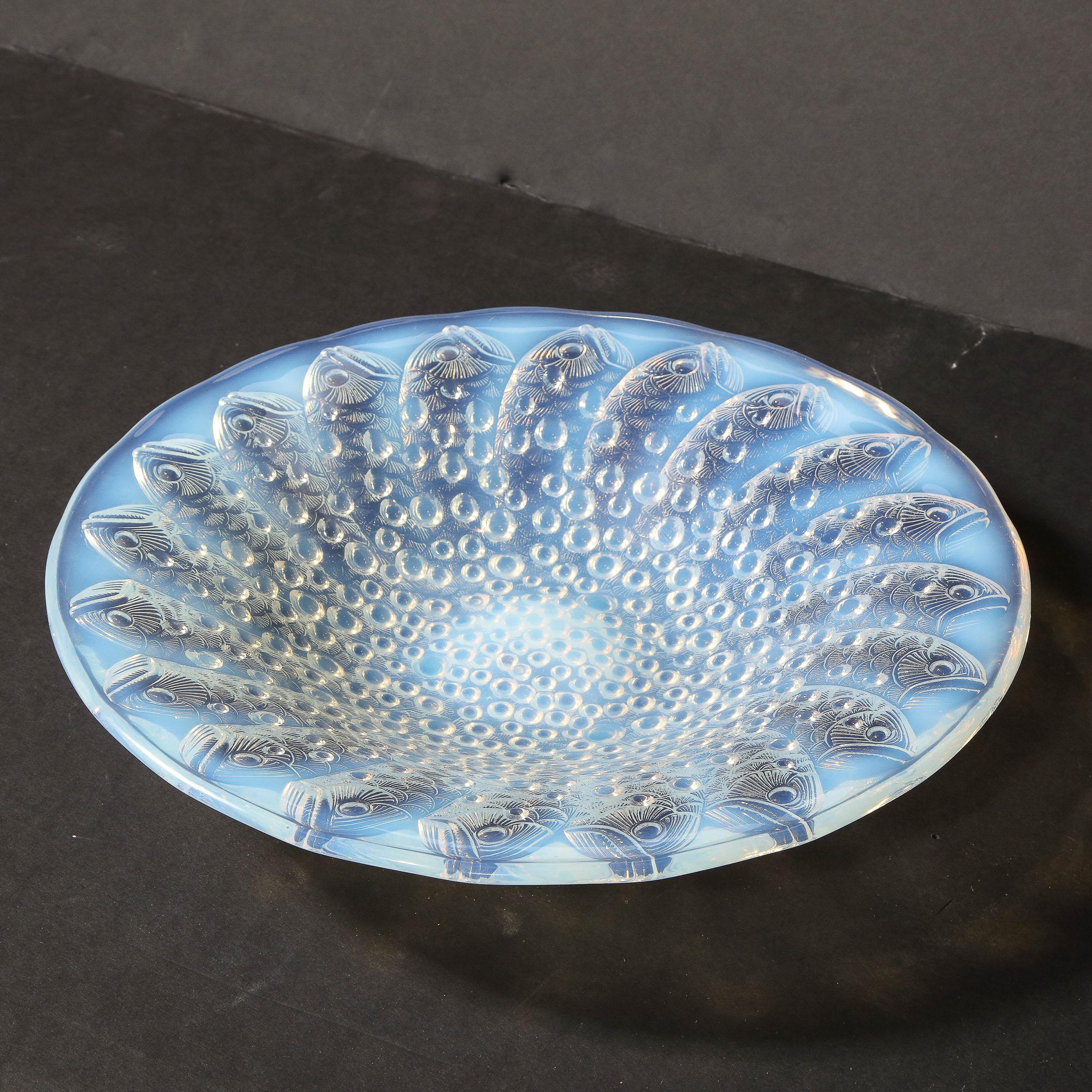 This stunning Art Deco center bowl was realized by the legendary maker Lalique in France circa 1925. Created in a beautiful opalescent glass, the piece offers a repeating concentric stylized fish motif as well as spherical detailing in relief. With