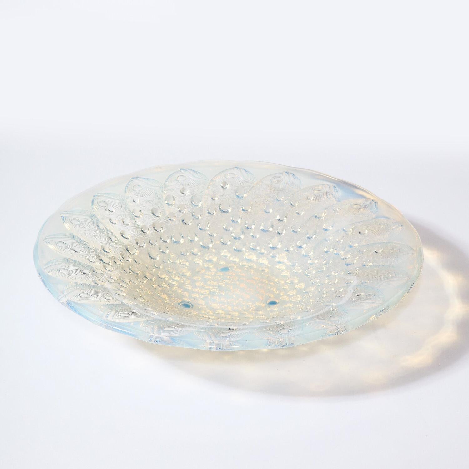 This stunning Art Deco center bowl was realized by the legendary maker Lalique in France circa 1925. Created in a beautiful opalescent glass, the piece offers a repeating concentric stylized fish motif as well as spherical detailing in relief. With