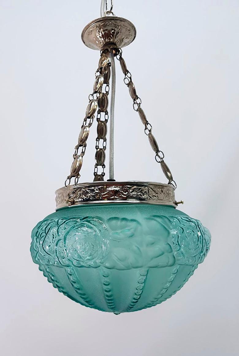 A unique Art Deco lamp that combines a glass tulip with a fretwork of brass, all subject by three chains of metal links.
This precious lamp is formed by a fretwork of brass engraved with figures of winged dragons, the finish of the metal is in aged
