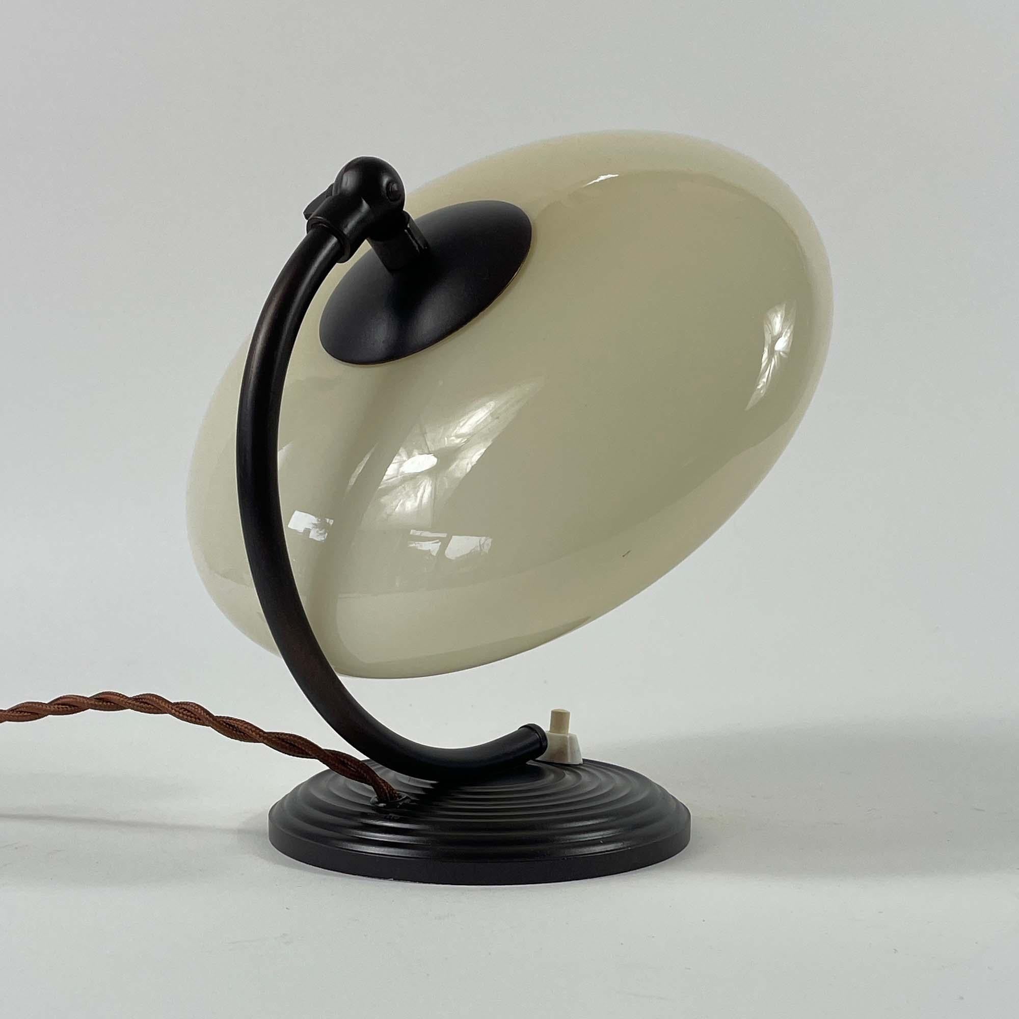 This Art Deco table lamp or bedside lamp was designed and manufactured in Germany during the Bauhaus Period in the 1920s to 1930s.

It features a cream / sand colored opaline glass UFO shaped lampshade and bronzed / burnished metal hardware.

The