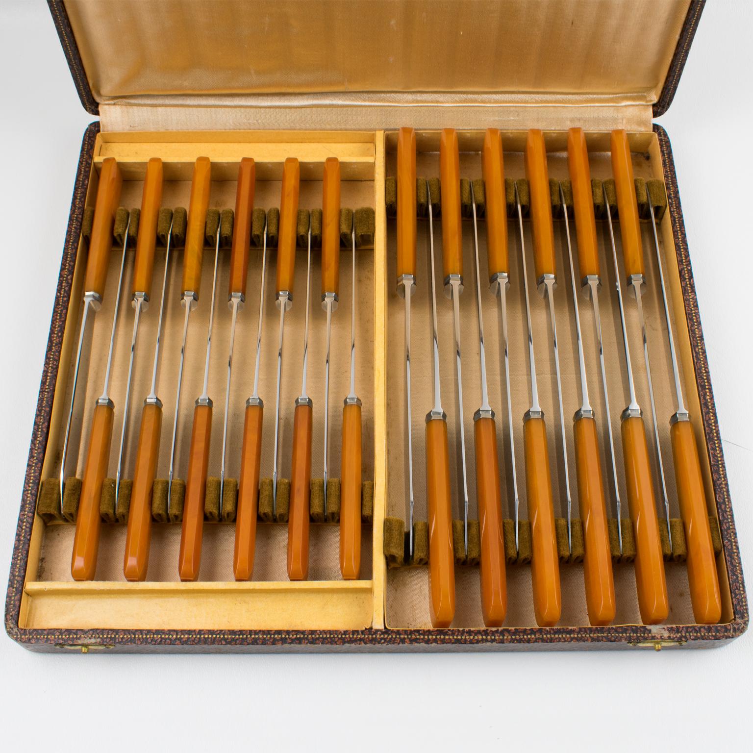 Este elegante juego de cuchillos francés Art Déco de baquelita y acero inoxidable conserva su caja original. Los dos conjuntos constan de 12 piezas cada uno, diseñadas específicamente para carne y fruta/queso. Las piezas presentan hojas de acero