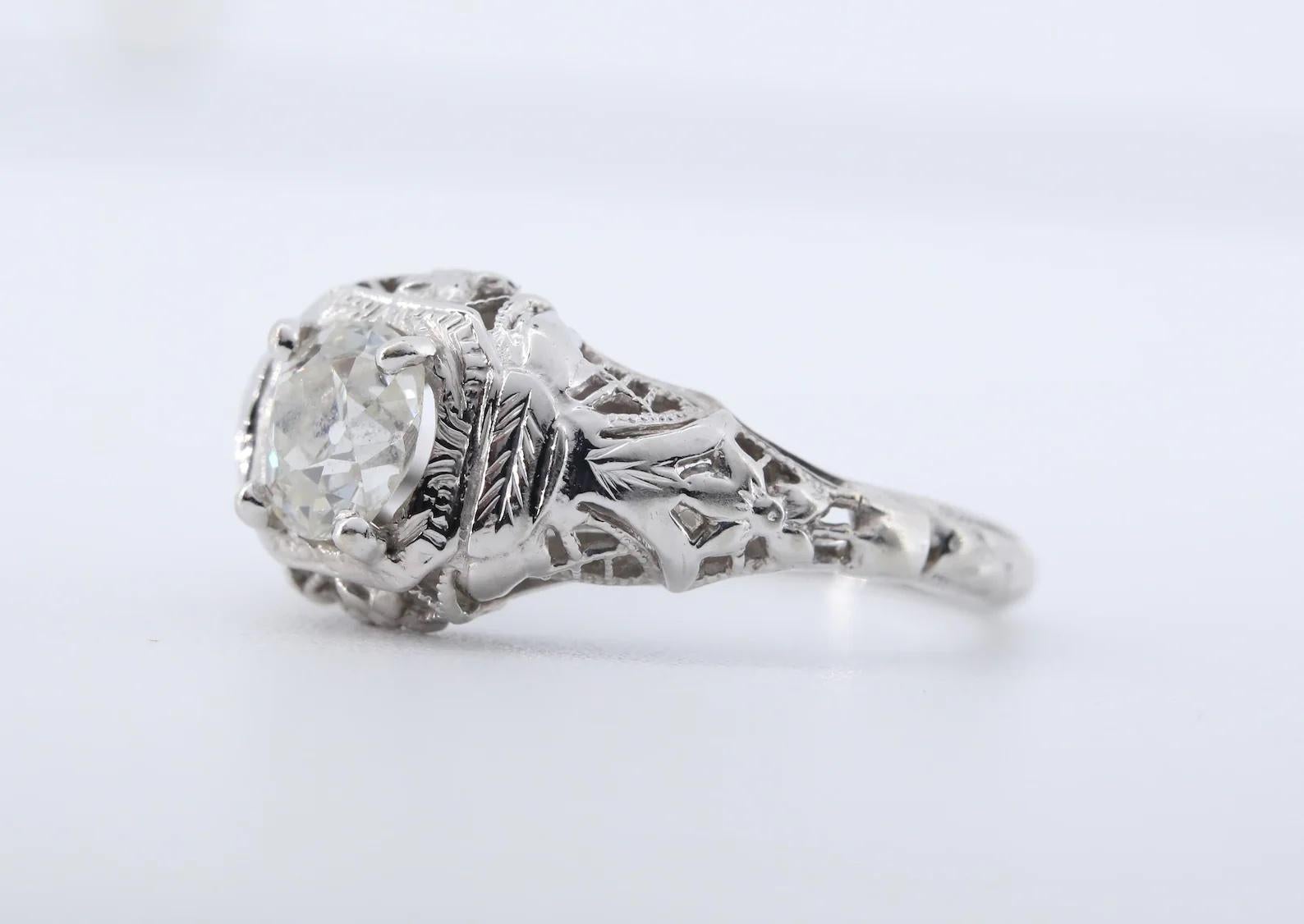 An Art Deco period old mine cut diamond solitaire engagement ring.

Centered with a 0.75 carat H color, SI1 clarity old mine cut cushion shaped diamond.

The die struck mounting embellished with pierced filigree work, and engraved detailing in the