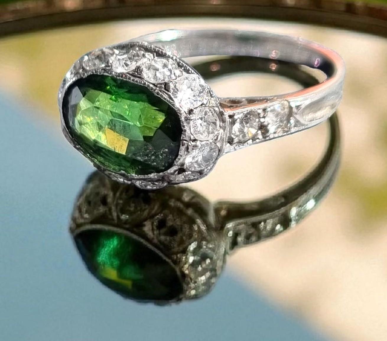 Anello originale Artful Green in platino con tormalina e diamanti, ca. 1920
Questo squisito anello Art Deco mette in mostra una vibrante tormalina verde dal taglio ovale, che misura circa (9,4 × 6,44 × 4,8 mm) 1,80 carati e irradia ricche sfumature