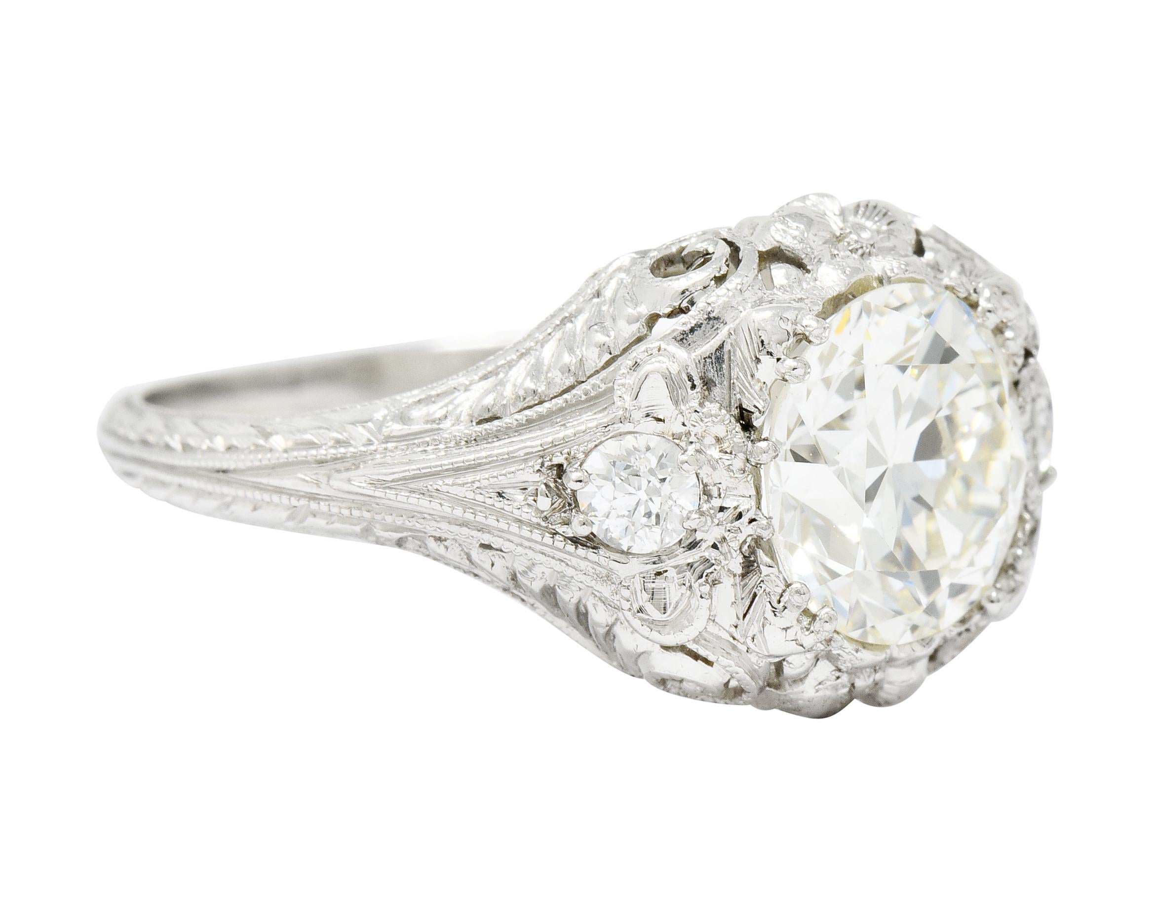 Centering an old European cut diamond weighing approximately 1.95 carats, L color with VS clarity

Set low in a decorative mounting featuring scrolled and scalloped shoulders with milgrain edges, orange blossom motif, and deeply engraved foliate
