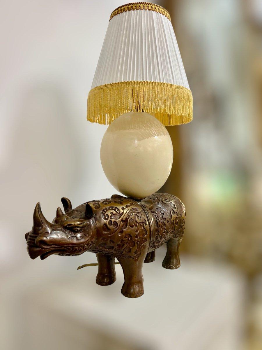 A unique curiosity cabinet-style table lamp crafted from a statue representing a rhinoceros, and topped with an imposing ostrich egg. The electrical wiring has been completely redone to meet contemporary electric standards. The dimensions of this