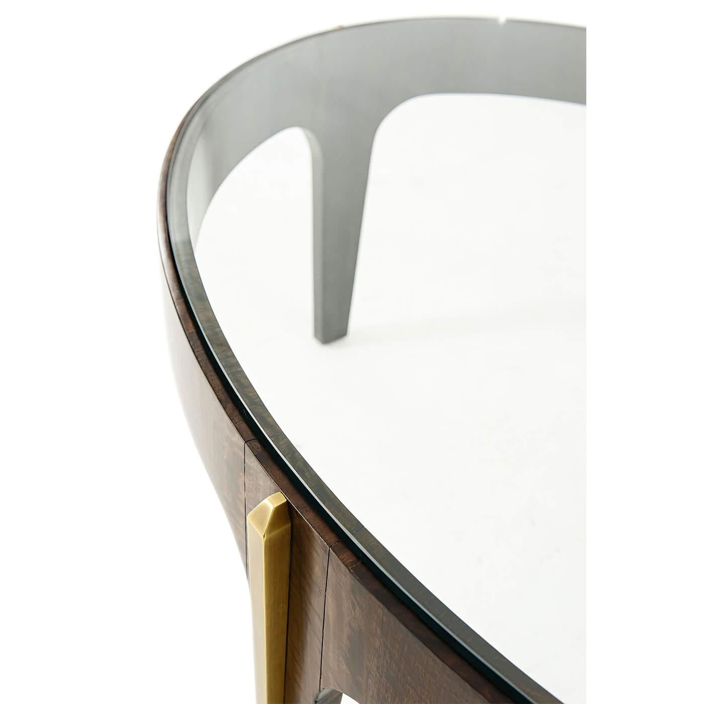 Une table de cocktail ovale de style Art Déco montée sur laiton, le plateau ovale en verre trempé dans une frise en placage, les pieds légèrement effilés avec des moulures en laiton. 

Dimensions : 48