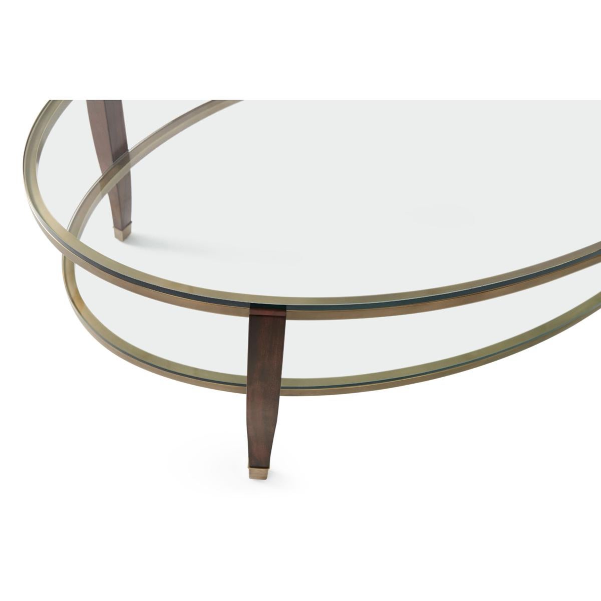 An oval two-tier glass top coffee table with mahogany supports accented with brass feet. It has two oval brass-bound tempered glass tiers. 

Dimensions: 52