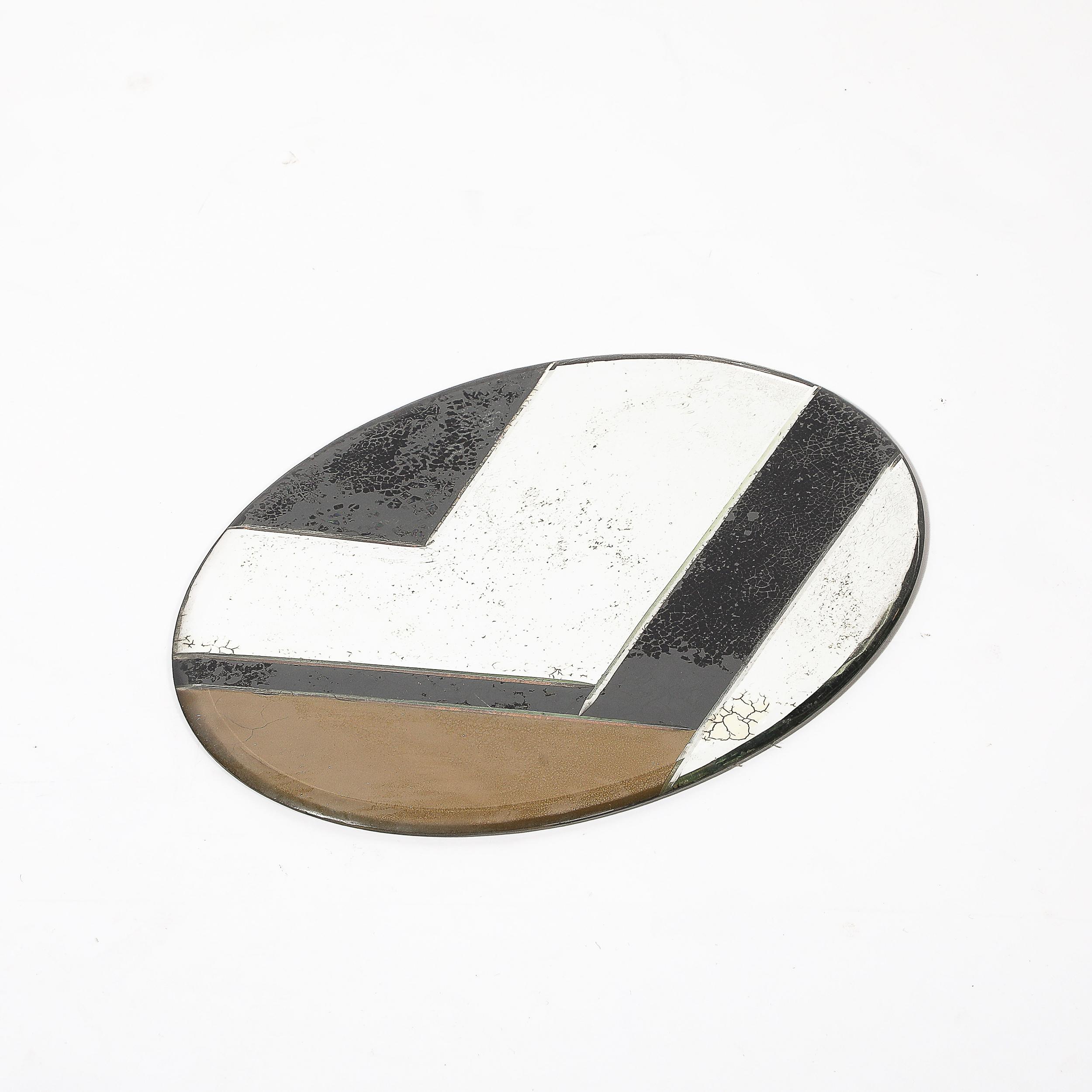 Cet extraordinaire plateau ovale Art déco, fabriqué en Amérique vers 1935, est une représentation frappante de l'élégance géométrique audacieuse qui définit cette période. Grâce à la technique sophistiquée de l'églomisé (peinture inversée et gravure