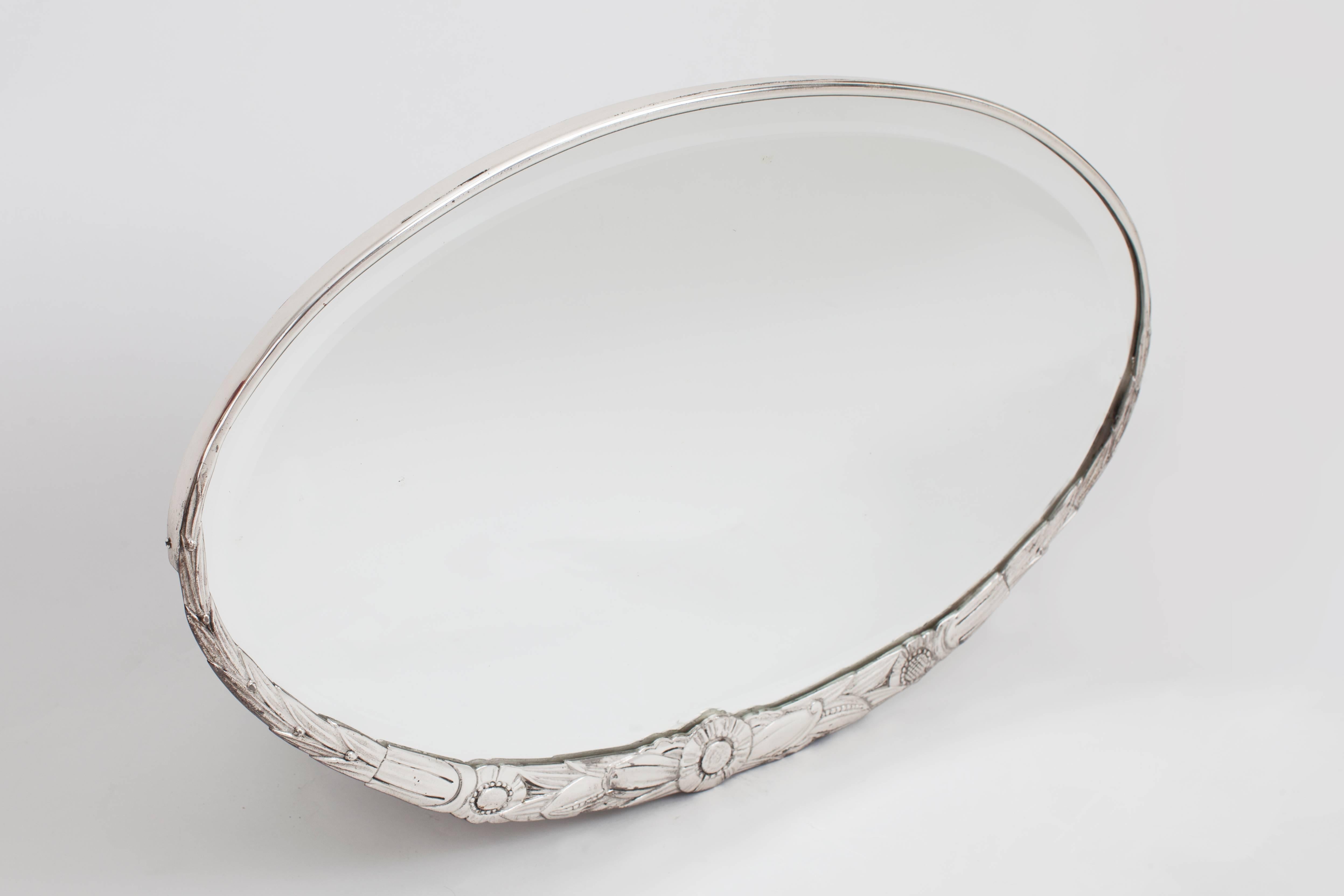 A delicate oval Art Deco Mirror with finely-incised floral and foliate décor of wheat shafts and poppies, in beautifully sculpted silvered brass with deeply bevelled original glass. France, 1930s.