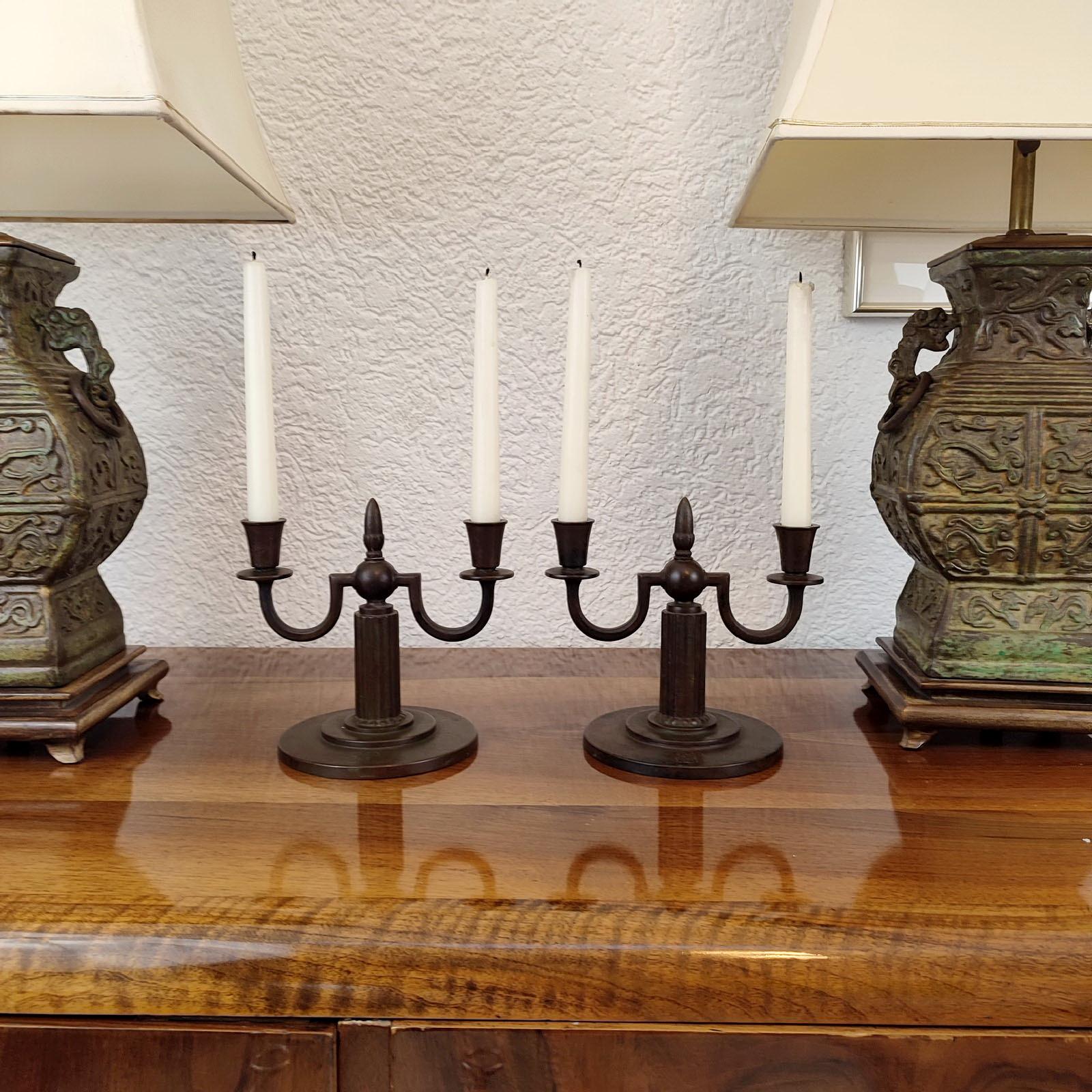 A pair of patinated bronze candle holders from Guldsmedsaktiebolaget - GAB, design attributed to Jacob Ängman. Early 1930s. Fluted stem on a round double stepped base, with two lights of 2cm. Monogrammed 