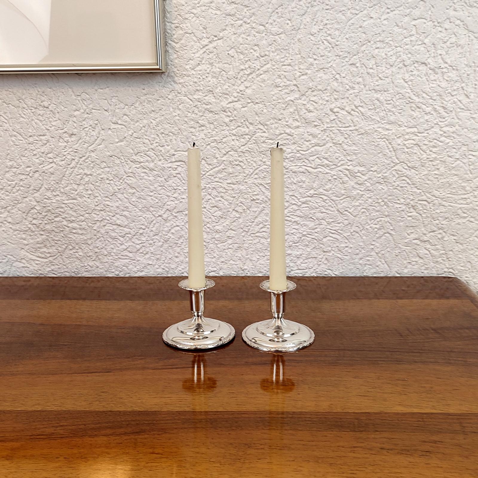 Pair of candlesticks, made of 830 silver. Round, ascending, partially rosette-like base, above it with a vase-shaped spout. Relief rocaille ribbon décor on the base and on the rim. Filled base for stability. Suitable for table candles up to 2.5 cm