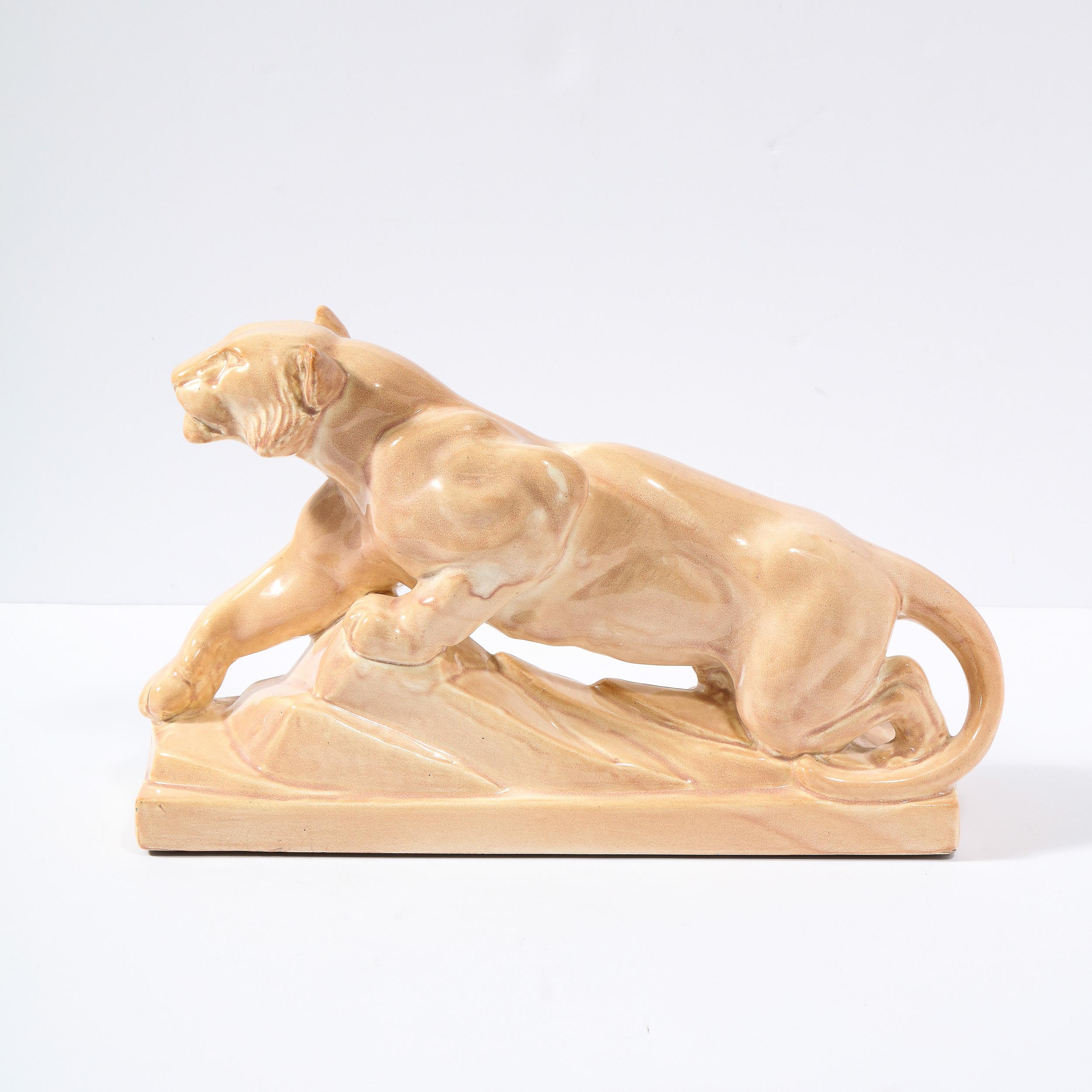 This stunning sculpture of an Art Deco Pouncing Tiger is realized in a pale terra-cotta glaze ceramic .It features a stylized Tiger on a stepped geometric base echoing the design of a cliff. The crackeluture of the glaze gives it that warm luminous