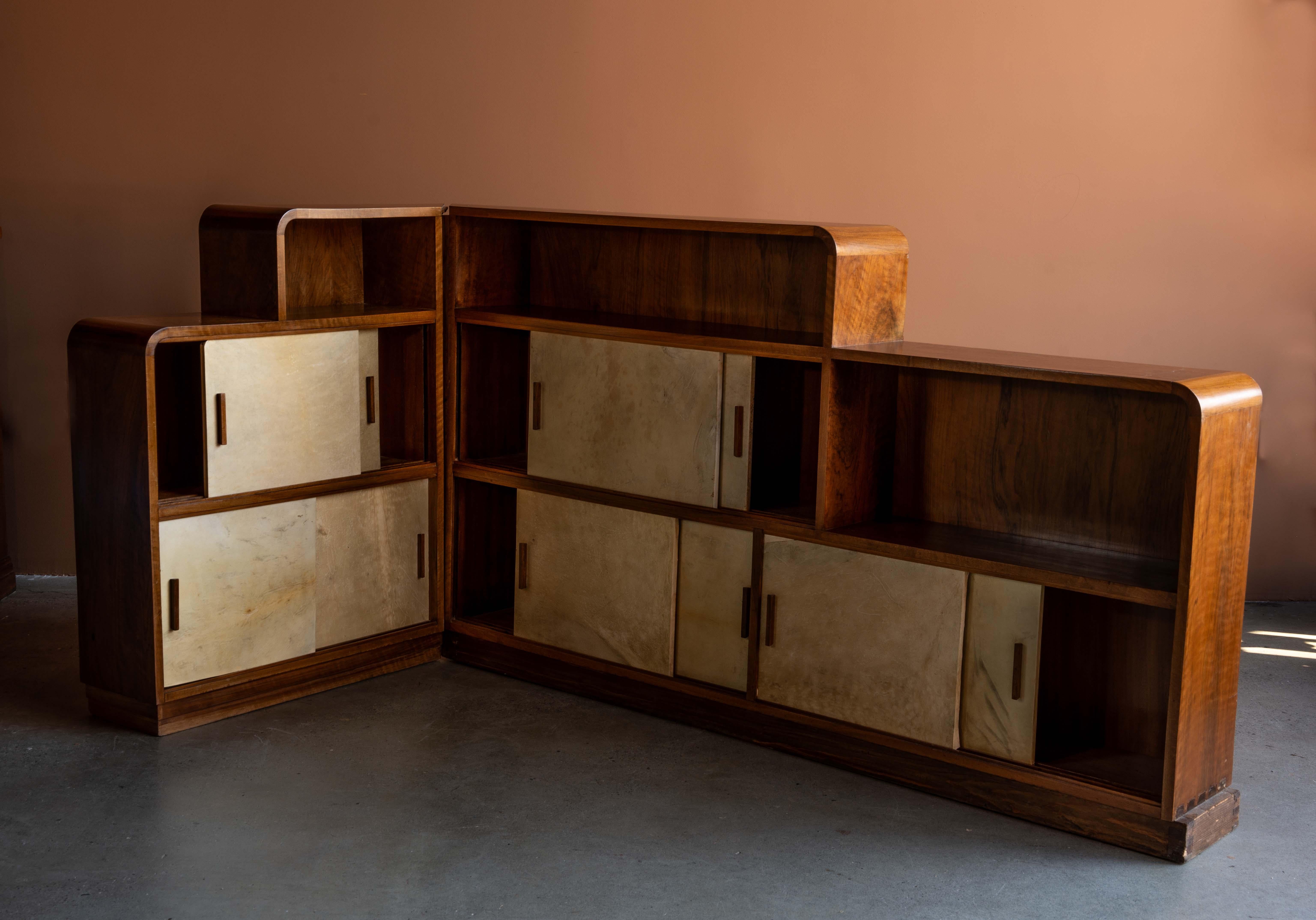 Credenza angolare in noce Art Déco con bordi arrotondati a cascata e ante scorrevoli con facciate in pergamena di capra patinata. Questo pezzo è composto da due sezioni che si incastrano senza soluzione di continuità in corrispondenza di un angolo a