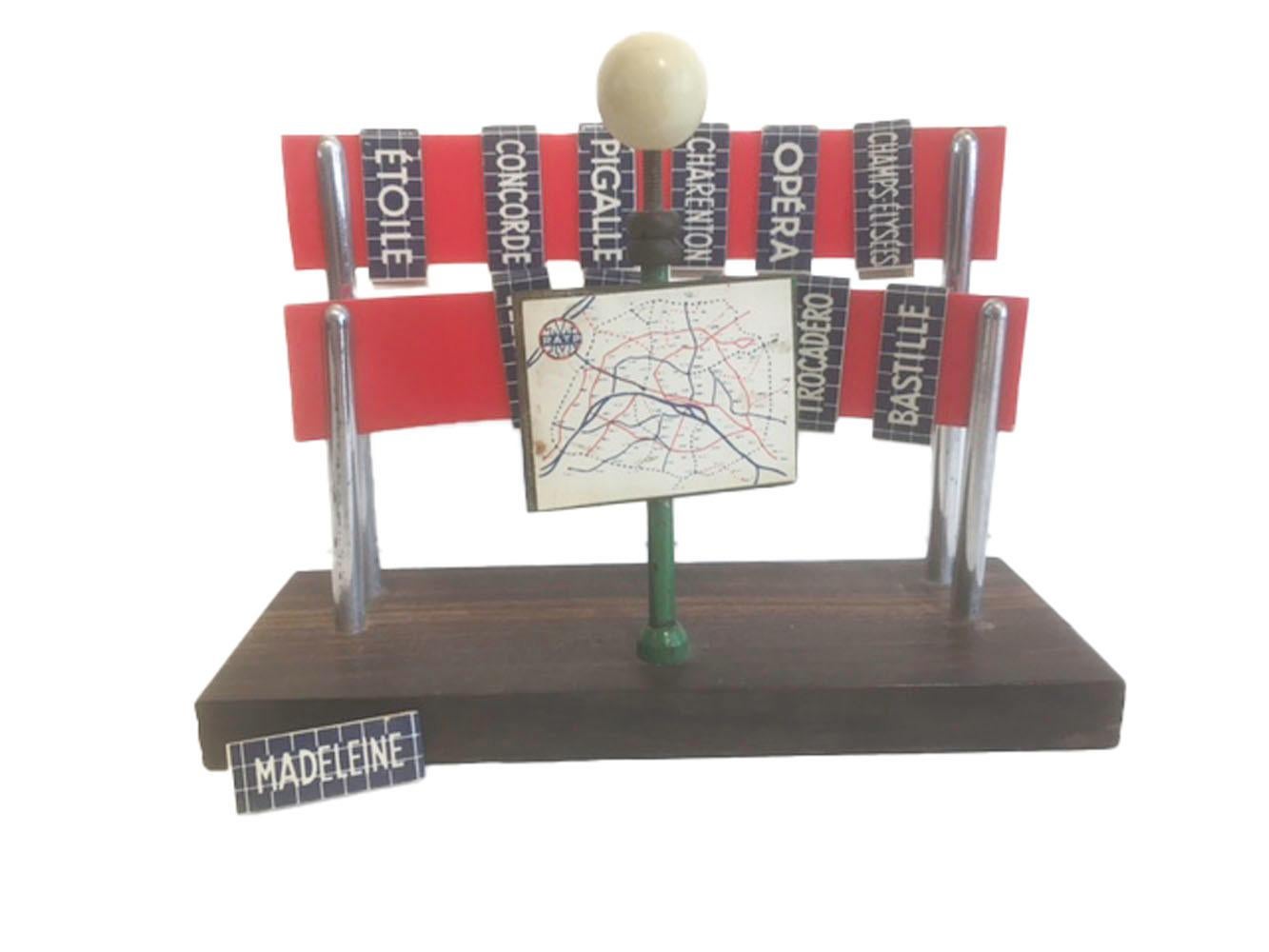 Art Deco drink markers with the names of Paris Metro stations. The celluloid markers printed with station names clip onto two celluloid banners raised on pairs of chrome posts behind a painted lamppost holding a map of the Paris Metro System. Clip a