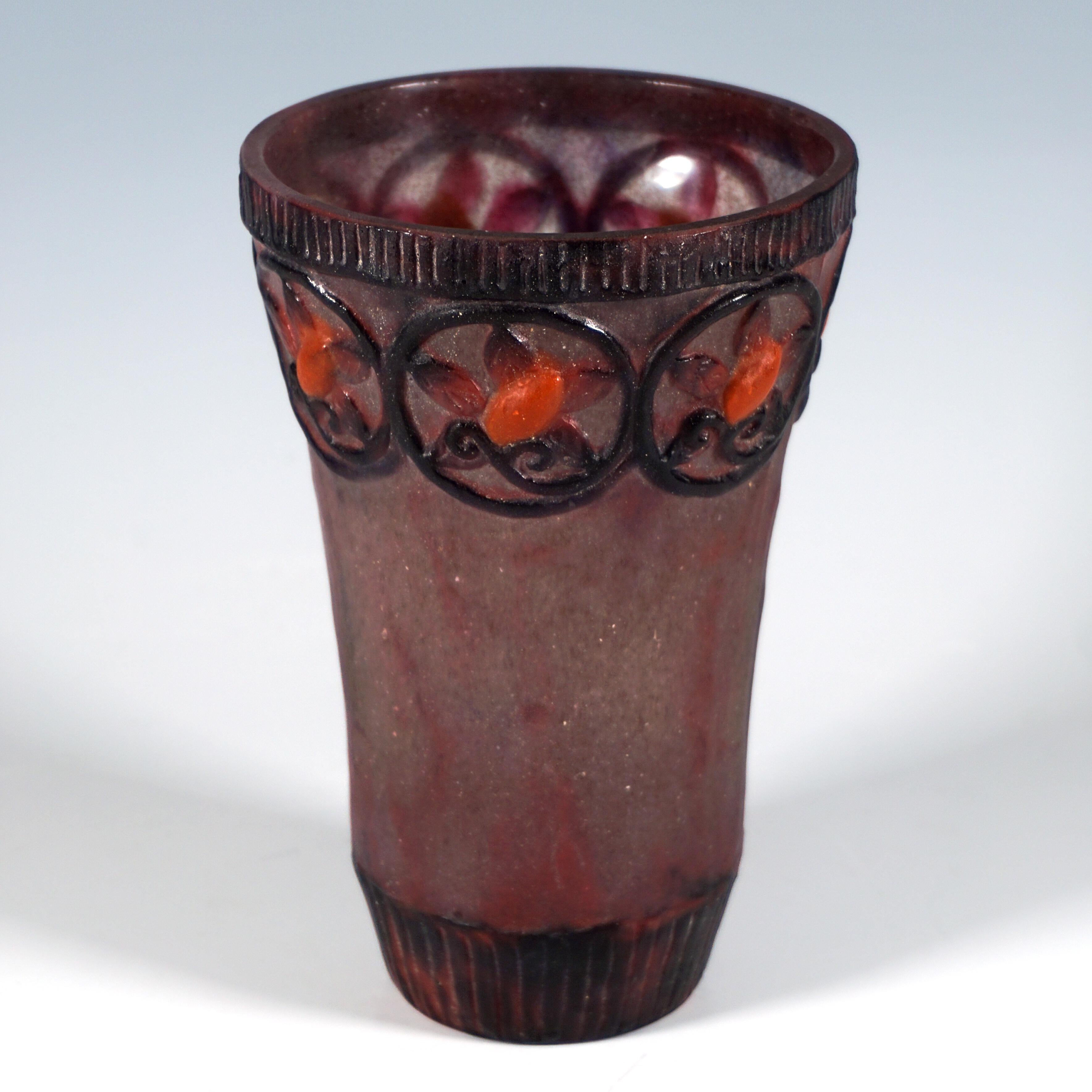 Slightly funnel-shaped beaker made of translucent pâte de verre with coloured powder meltings in burgundy red, light green and black, ribbed decorative strips on the upper and lower edges, and a decorative strip in relief at 
the top with