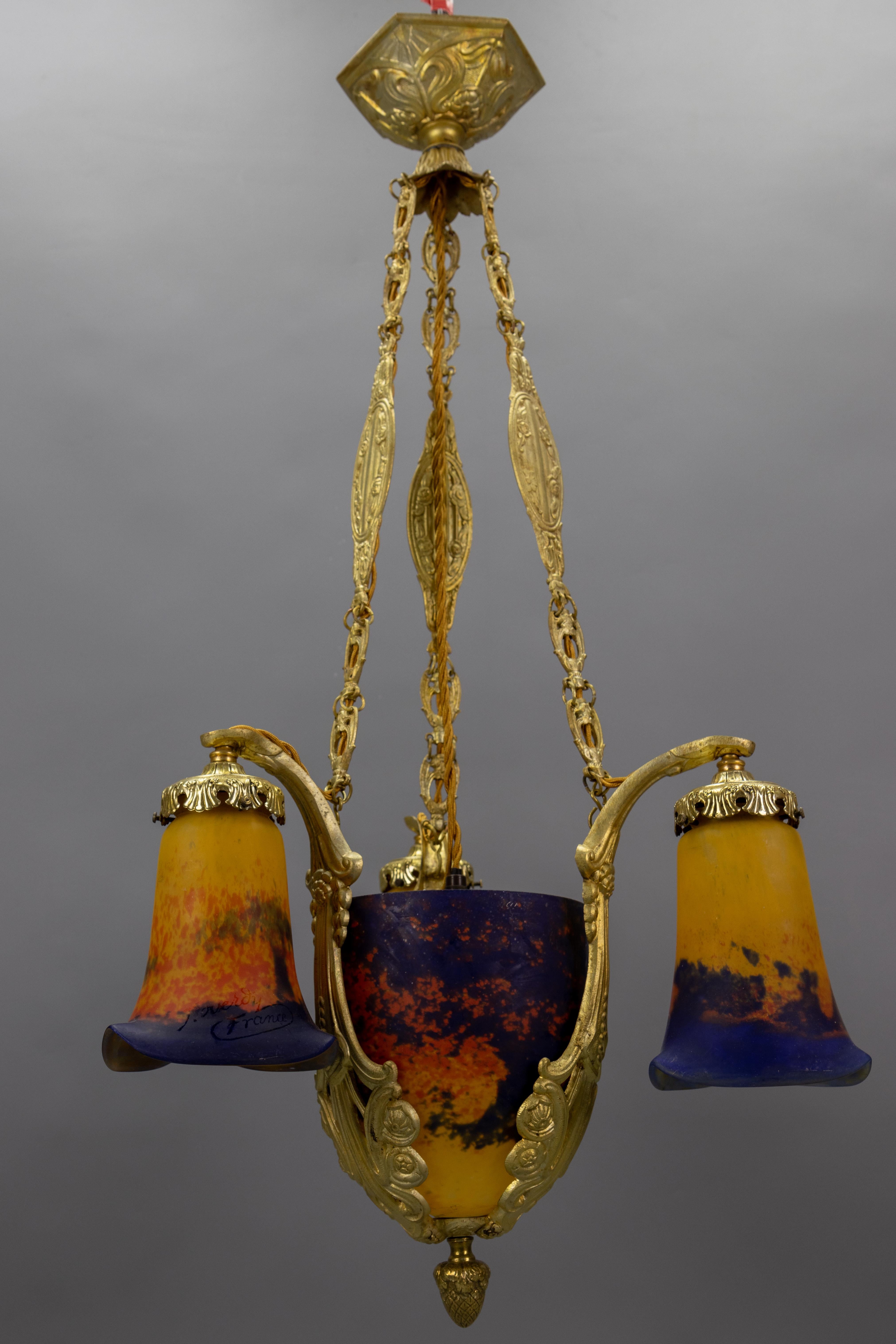 Art Deco pâte de verre glass and bronze four-light chandelier by Jean Noverdy France, circa the 1920s.
This splendid French Art Deco period chandelier features a central, beautifully shaped “Pâte de Verre” glass lampshade in dark yellow, red, and