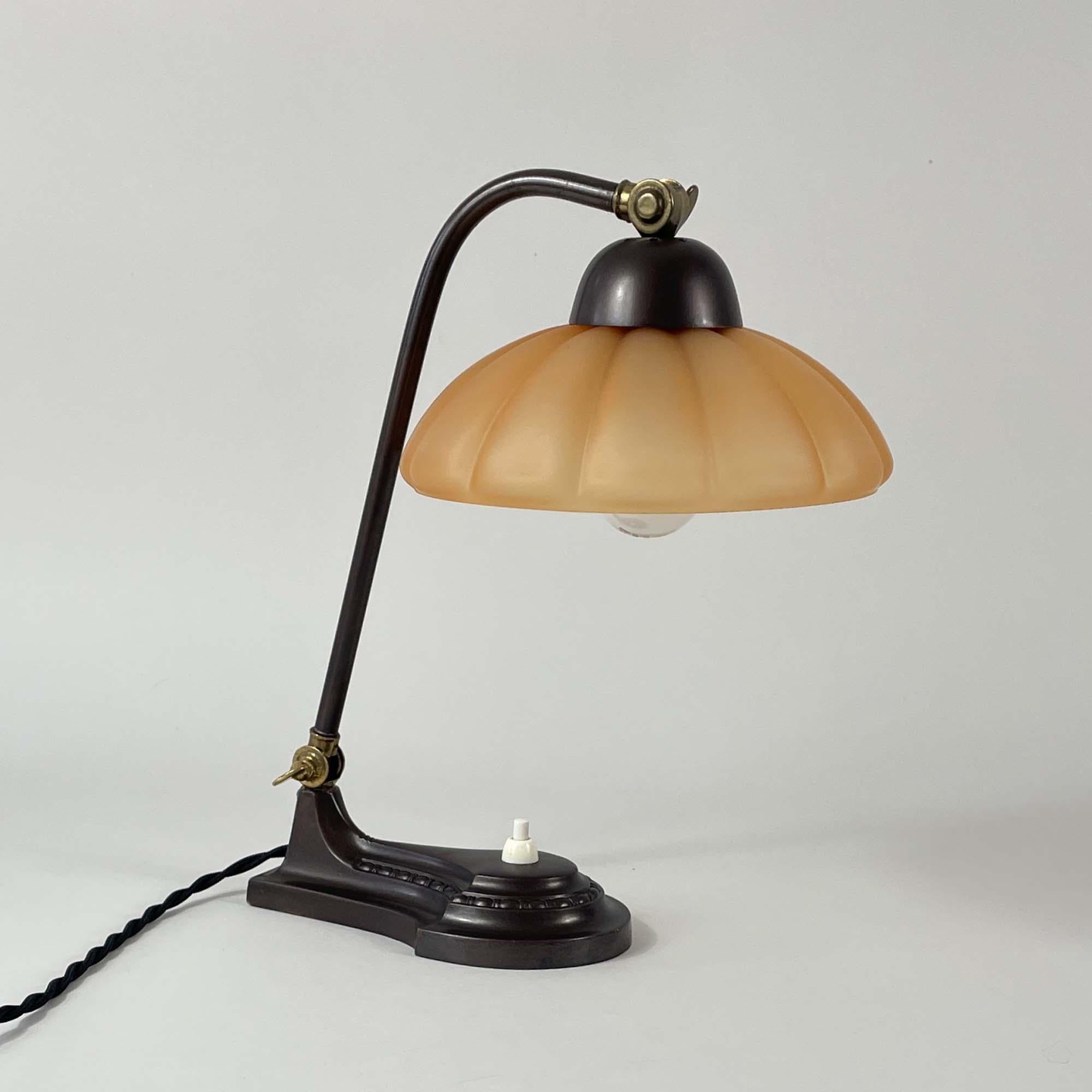 This elegant vintage table lamp was designed and manufactured in Sweden during the Swedish Grace period. It features a soft, translucent dark peach colored glass lampshade (Havanna Glass) and bronzed brass hardware.

The base has a streamlined