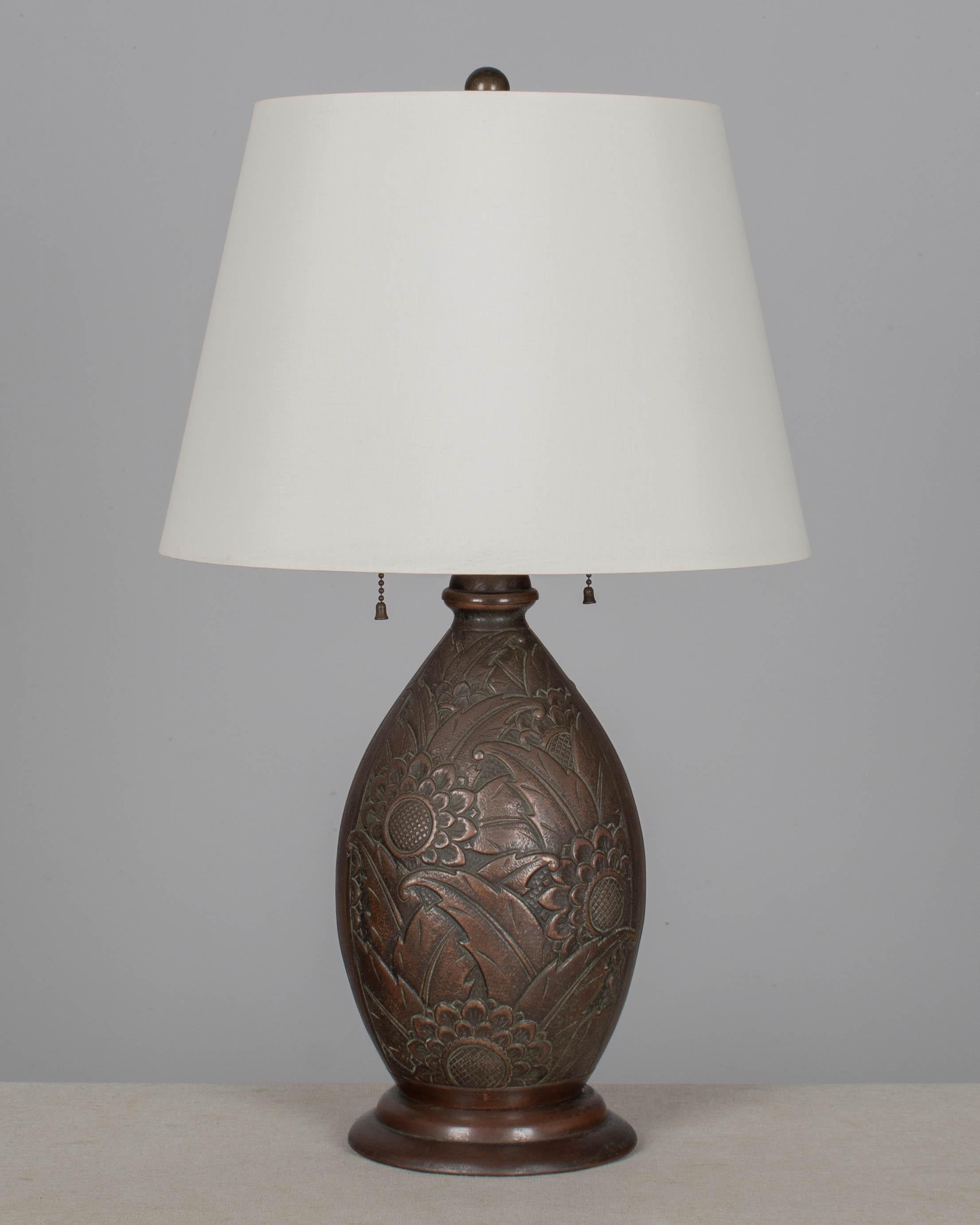 Lámpara de sobremesa Art Decó de latón patinado con estilizado relieve floral. En buen estado, con una bonita pátina de color bronce. Enchufe doble original con cadenas de tracción, recableado con clavija original. Alrededor de 1930-1940. La