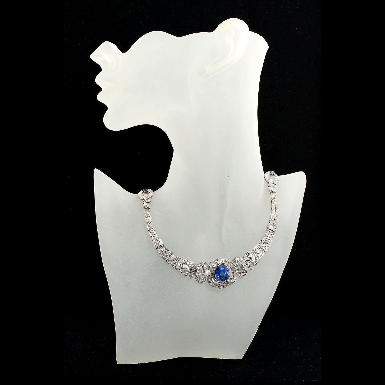 This remarkably well preserved Art Deco period necklace is a rare piece of art.  Featuring a unique modified pear shape Natural Blue Sapphire bezel set within diamond and platinum handmade curving and festooned metal work and inlaid with approx.