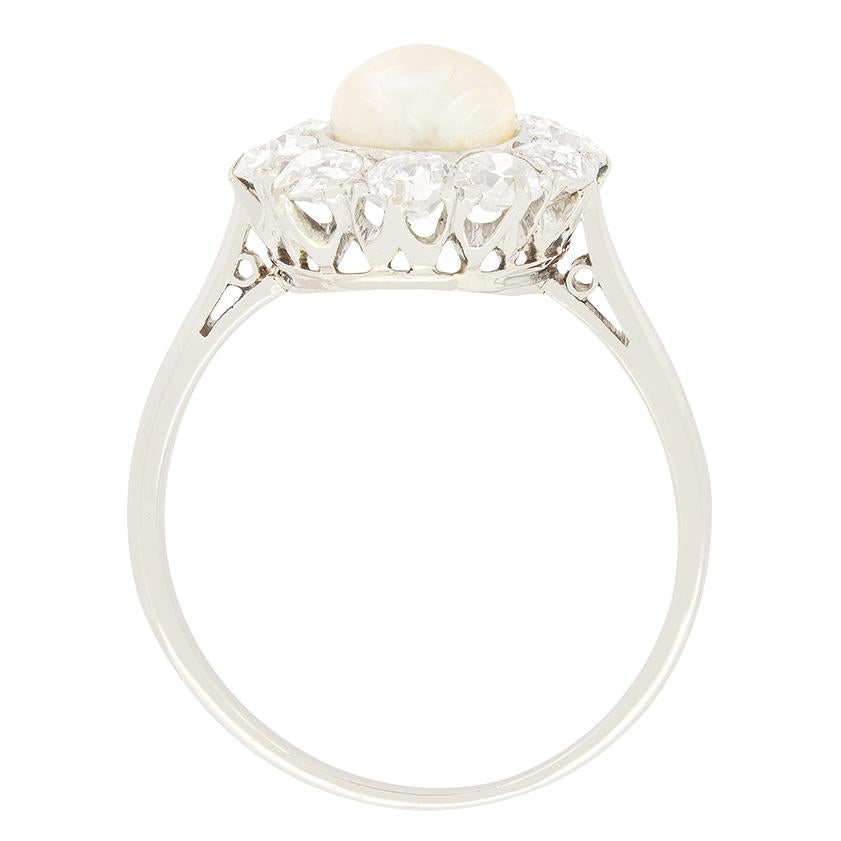 Una splendida perla naturale è circondata da diamanti antichi in questo anello a grappolo del periodo Art Déco. La perla è di dimensioni impressionanti: 6,4 mm per 5,8 mm. L'aureola di diamanti ammonta a 1,00 carati per un totale di dieci diamanti.