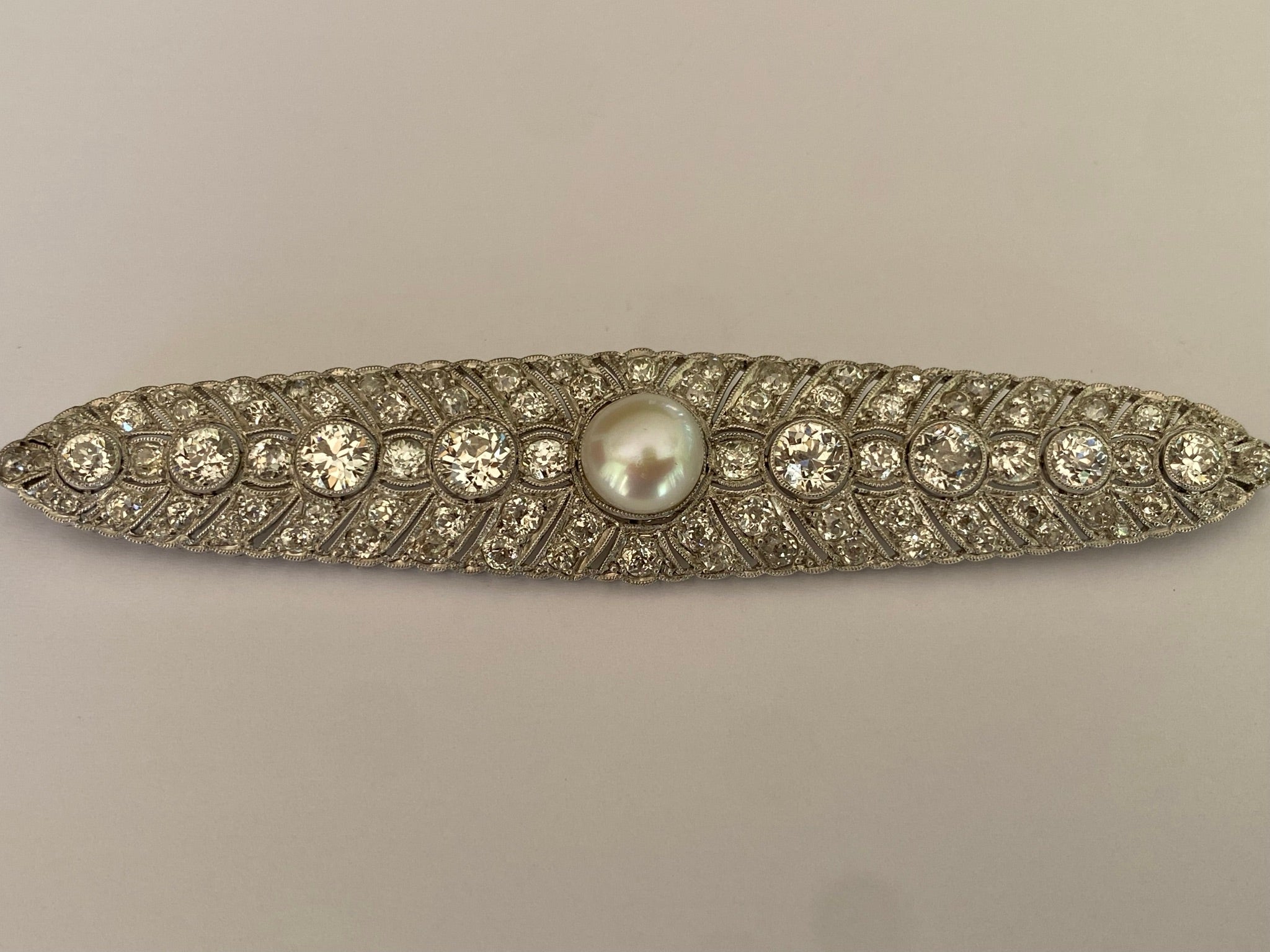 Diese exquisite, in den 1920er Jahren aus Platin gefertigte Art-Déco-Brosche zeigt eine 9 mm große, blasenförmige weiße Perle, die in der Mitte einer Reihe von acht Diamanten mit altem europäischem Schliff von insgesamt ca. 4,00 Karat sitzt. Sie ist