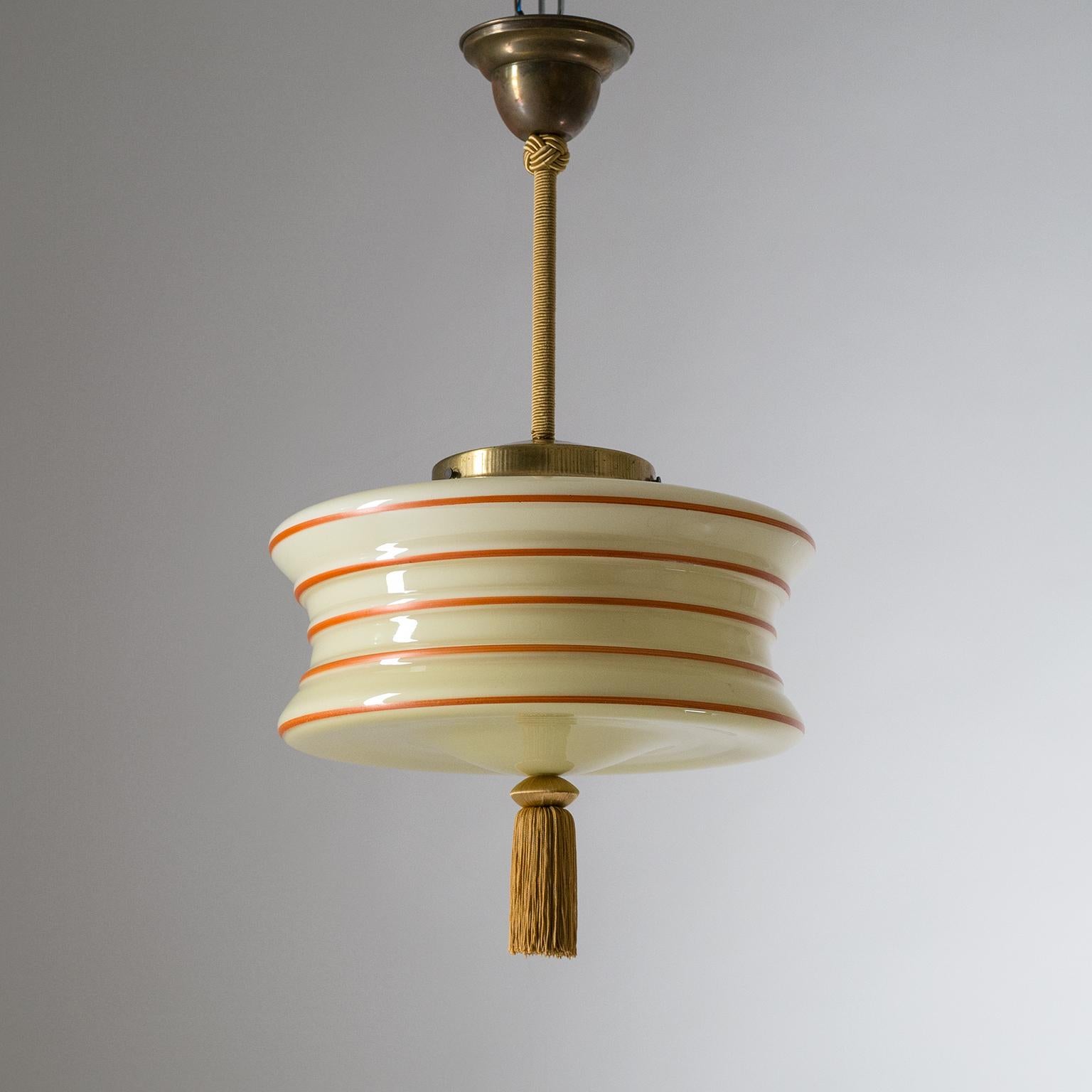 Enameled glass pendant from the 1930s. The uniquely shaped glass diffuser is made of Ivory tinted glass with a white inner casing and red hand-painted lines, emphasizing the structured silhouette. Brass hardware with covered stem and a tassel at the