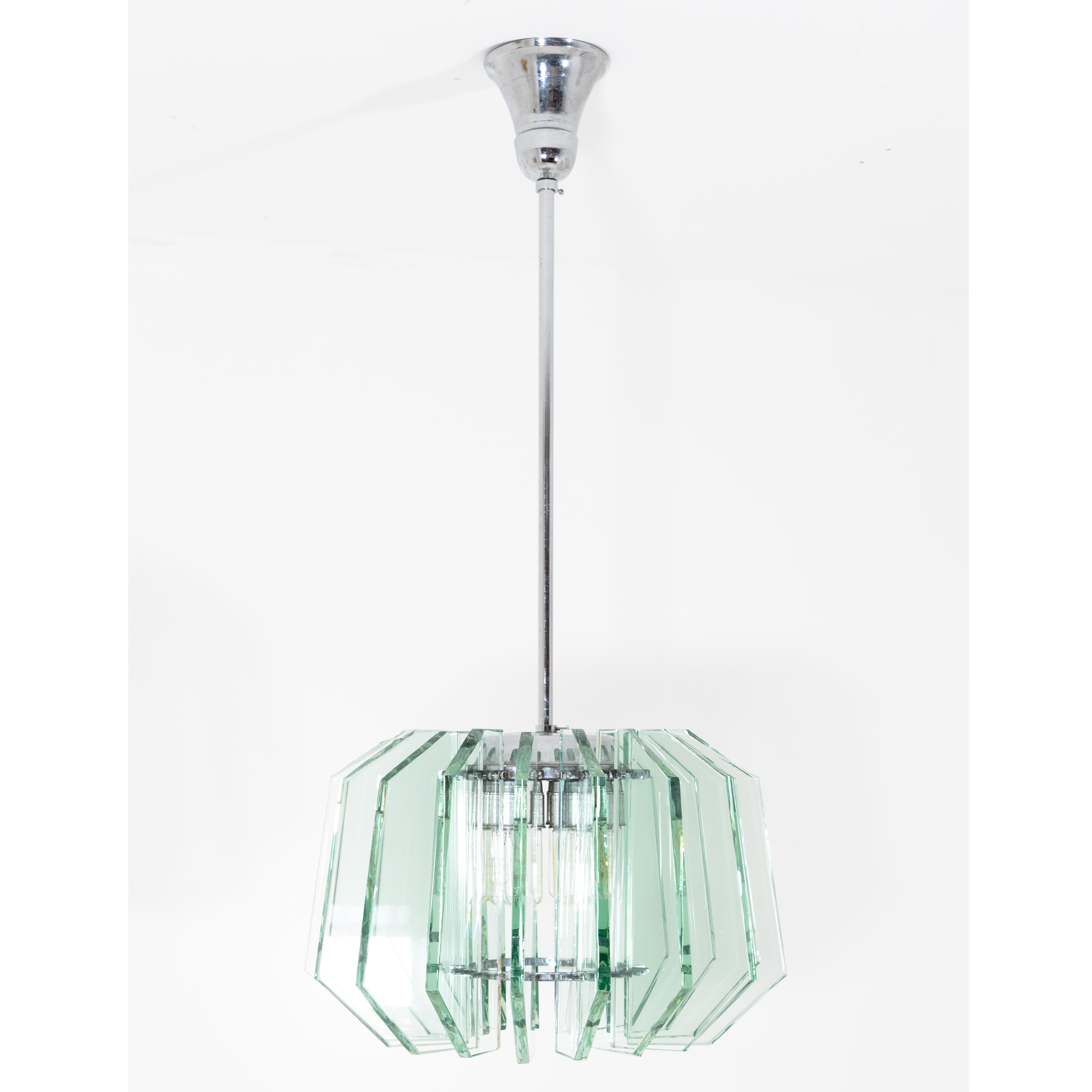Art Deco pendant lamp suspended from a long chrome-plated rod. Around the centre are 18 green-tinted thick glass panes with beveled corners. The panes have rough edges in some places. The lamp is correspondingly illuminated by 18 radially arranged