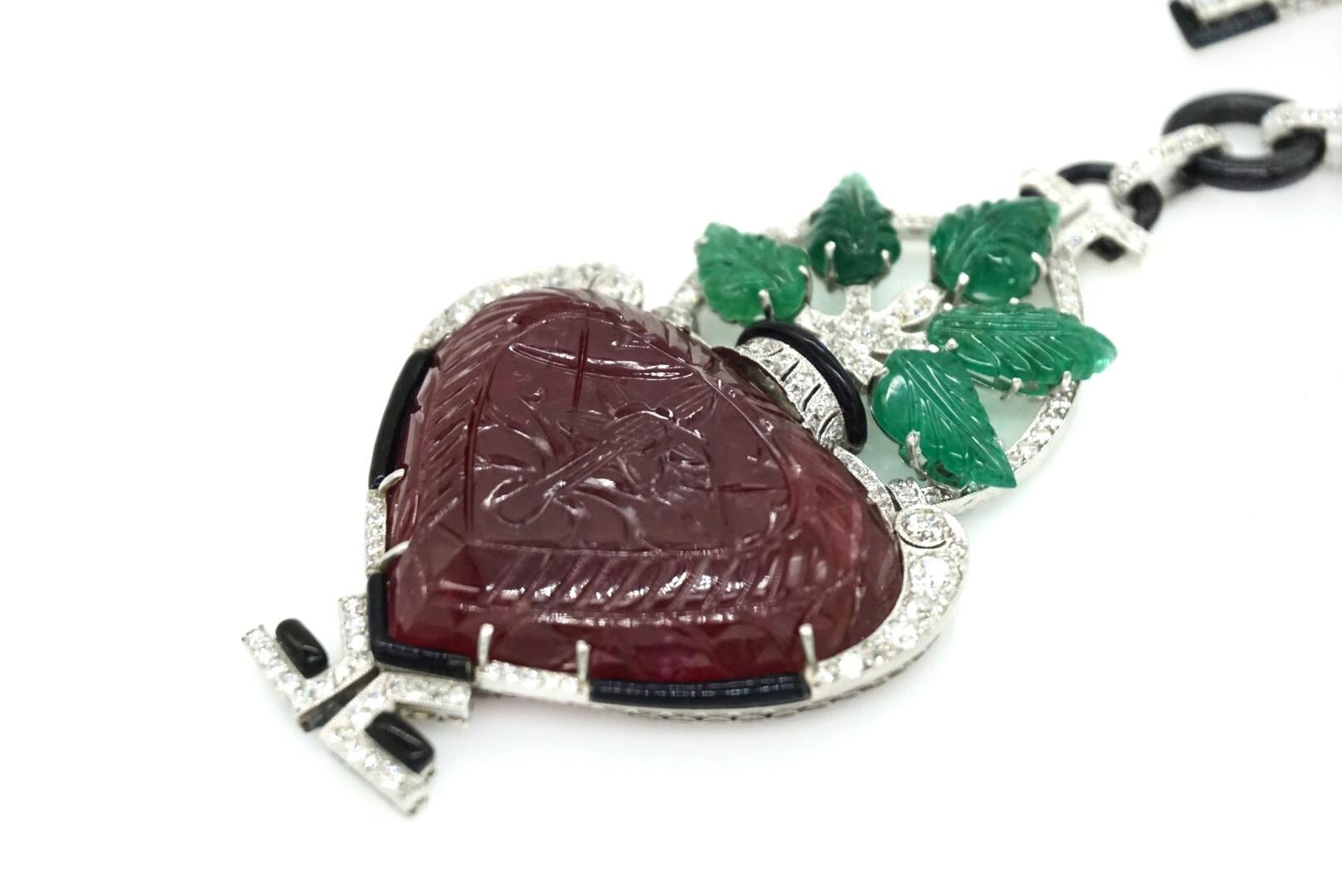 An Art Deco Pendant/Lapel Brooch mounted in platinum, with onyx and old-cut diamonds, with carved leaf emeralds and a large carved heart-shaped ruby. Made in Austria,  circa 1925.
